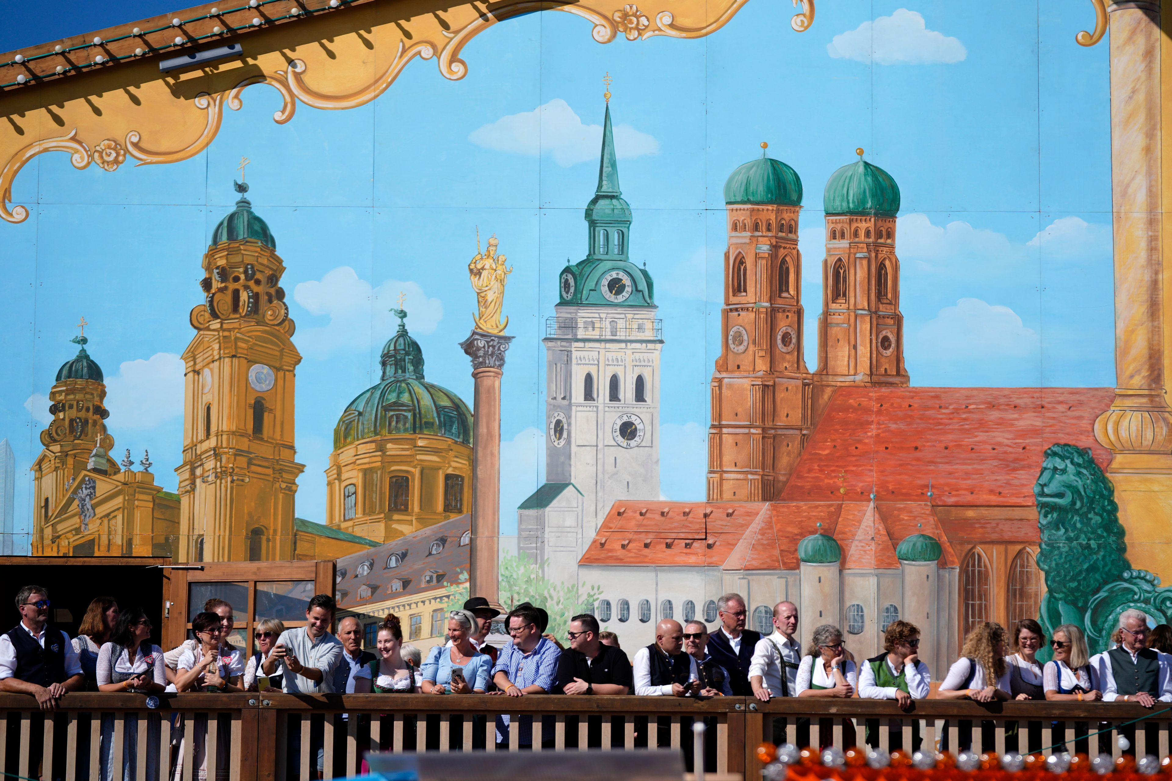 Visitors await the start of the 189th 'Oktoberfest' beer festival in front of paintings showing Munich landmarks in Munich, Germany, Saturday, Sept. 21, 2024. (AP Photo/Matthias Schrader)