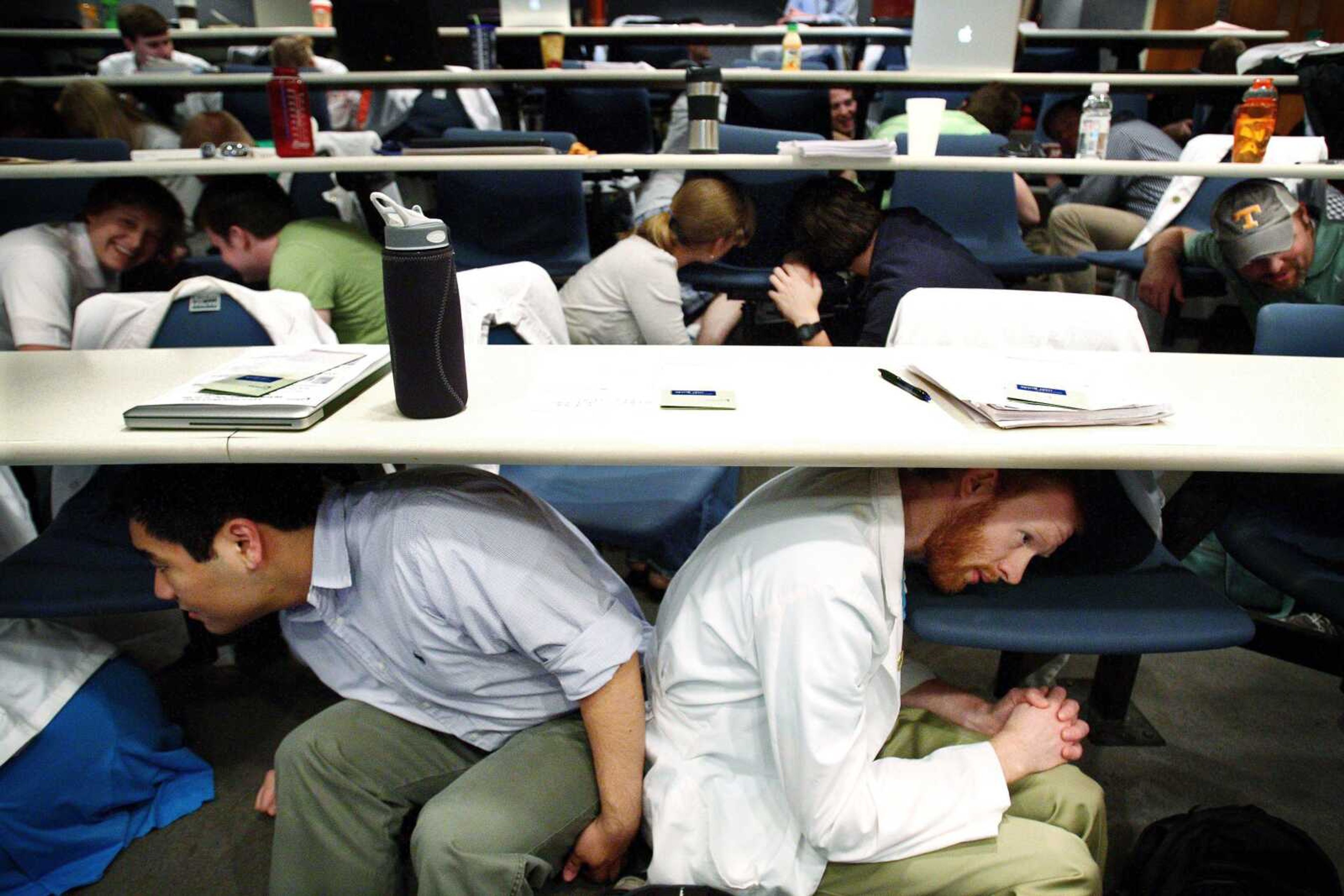 Third-year medical students Alex Chinn, left, and Chris Bates at University of Tennessee Health Science Center in Memphis, Tenn., are among the students in a lecture class that duck under the desk behind them during an earthquake drill Thursday. The students and faculty across the campus joined people in eight states for a simultaneous drill. (Mike Brown ~ The Commercial Appeal)