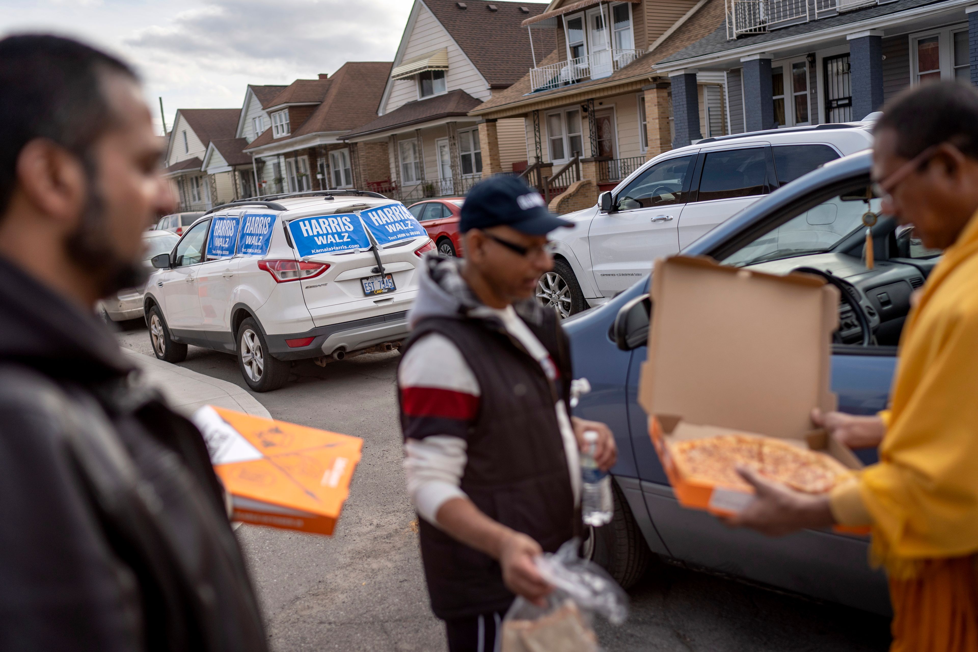 Posters for Democratic presidential nominee Vice President Kamala Harris are seen outside a polling site as Dharmananda Mahaprabu Barua, right, a Buddhist monk and supporter of Republican presidential nominee former President Donald Trump, brings pizza to fellow Trump supporters campaigning, Tuesday, Nov. 5, 2024, in Hamtramck, Mich. (AP Photo/David Goldman)