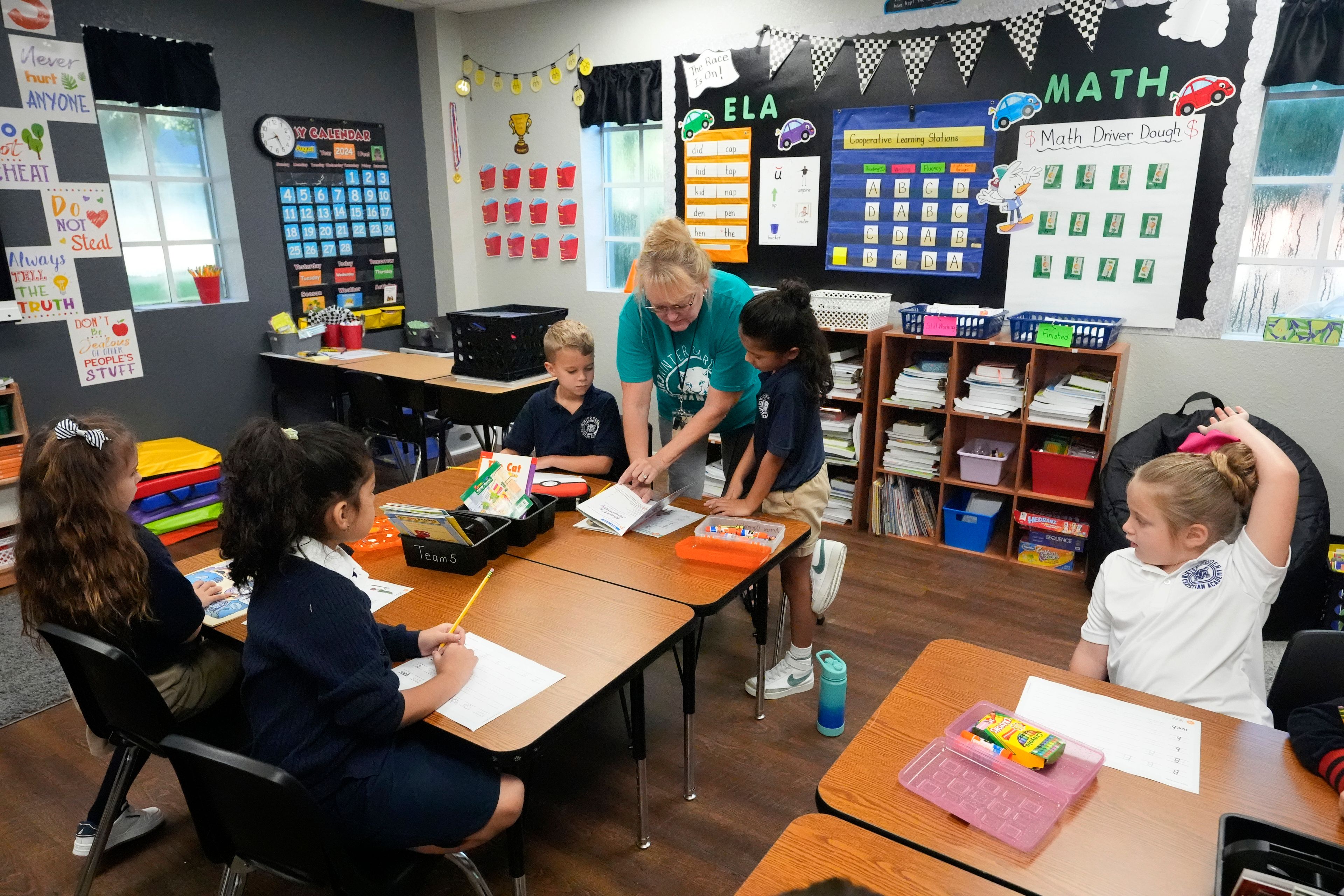 First grade teacher Sharon Parsons, back center, helps her students with a lesson at the Winter Garden Christian Academy Thursday, Aug. 29, 2024, in Winter Garden, Fla. (AP Photo/John Raoux)