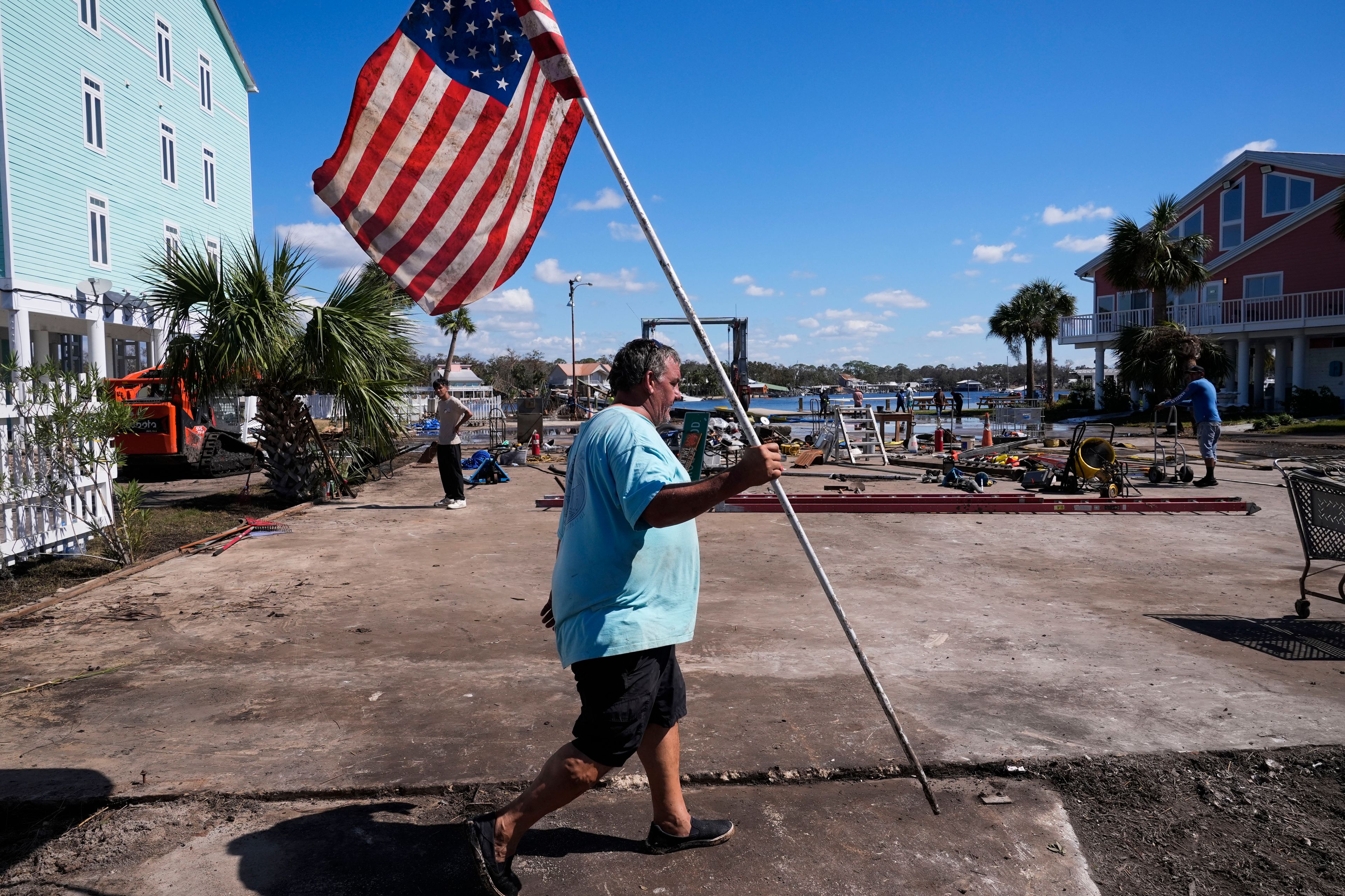 Daniel Dickert walks to plant an American flag on is property were his boat shed was destroyed and his home damaged in the aftermath of Hurricane Helene, in Jena, Fla., Sunday, Sept. 29, 2024. (AP Photo/Gerald Herbert)