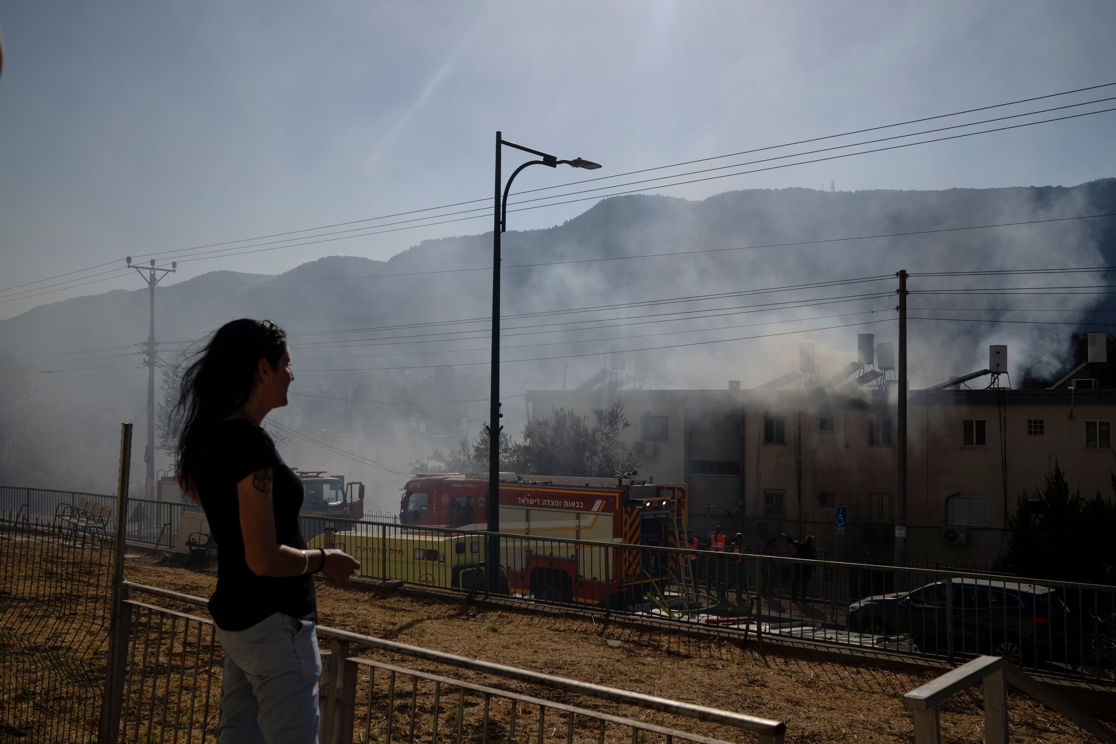 A woman looks on as firefighters work to extinguish a fire after a rocket, fired from Lebanon, hit a residential building in Kiryat Shmona, northern Israel, Wednesday, Oct. 9, 2024. (AP Photo/Leo Correa)