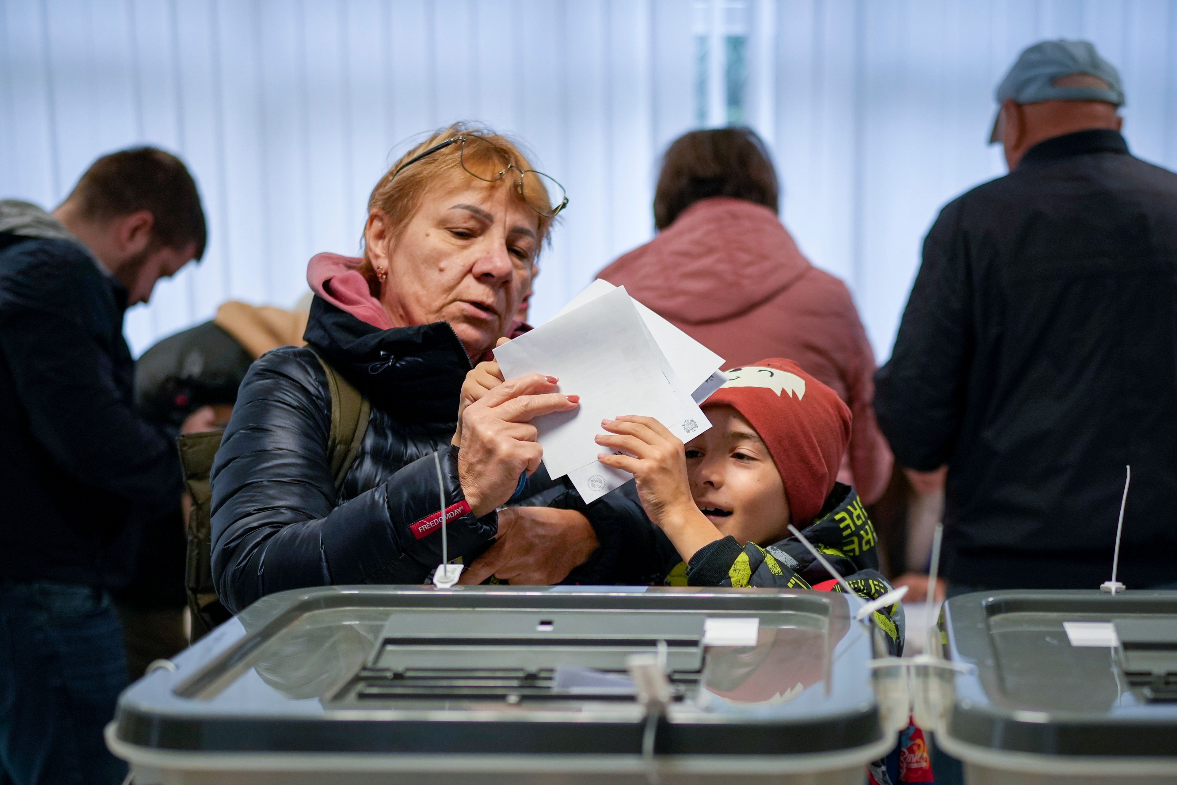 A woman hands a child her vote to cast in Chisinau, Moldova, Sunday, Oct. 20, 2024, during a presidential election and a referendum on whether to enshrine in the Constitution the country's path to European Union membership. (AP Photo/Vadim Ghirda)