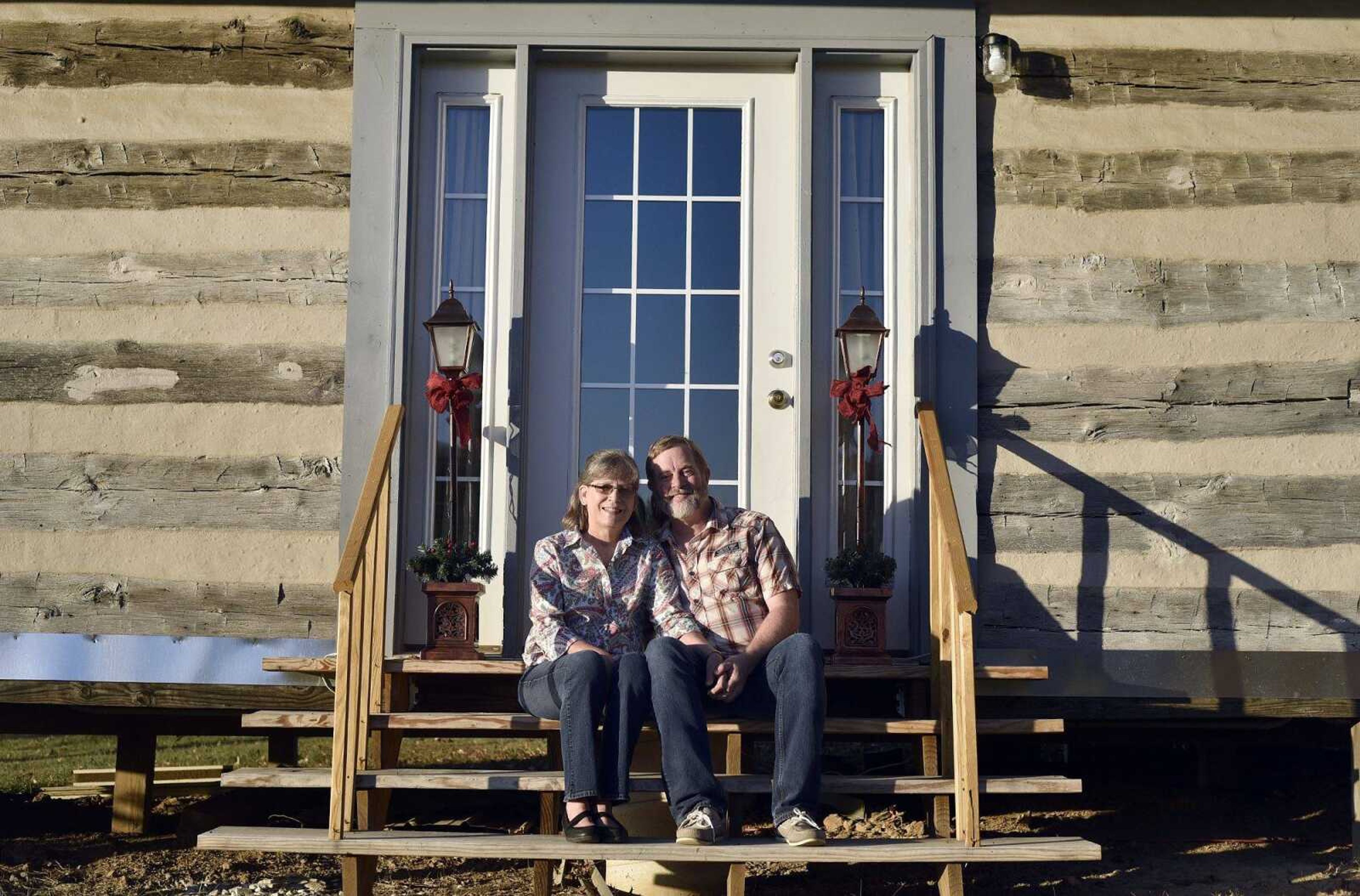 Kim and Earl Bennett sit outside the log cabin they rebuilt in Jackson. The log cabin was built by Kim's great-grandfather in 1901.