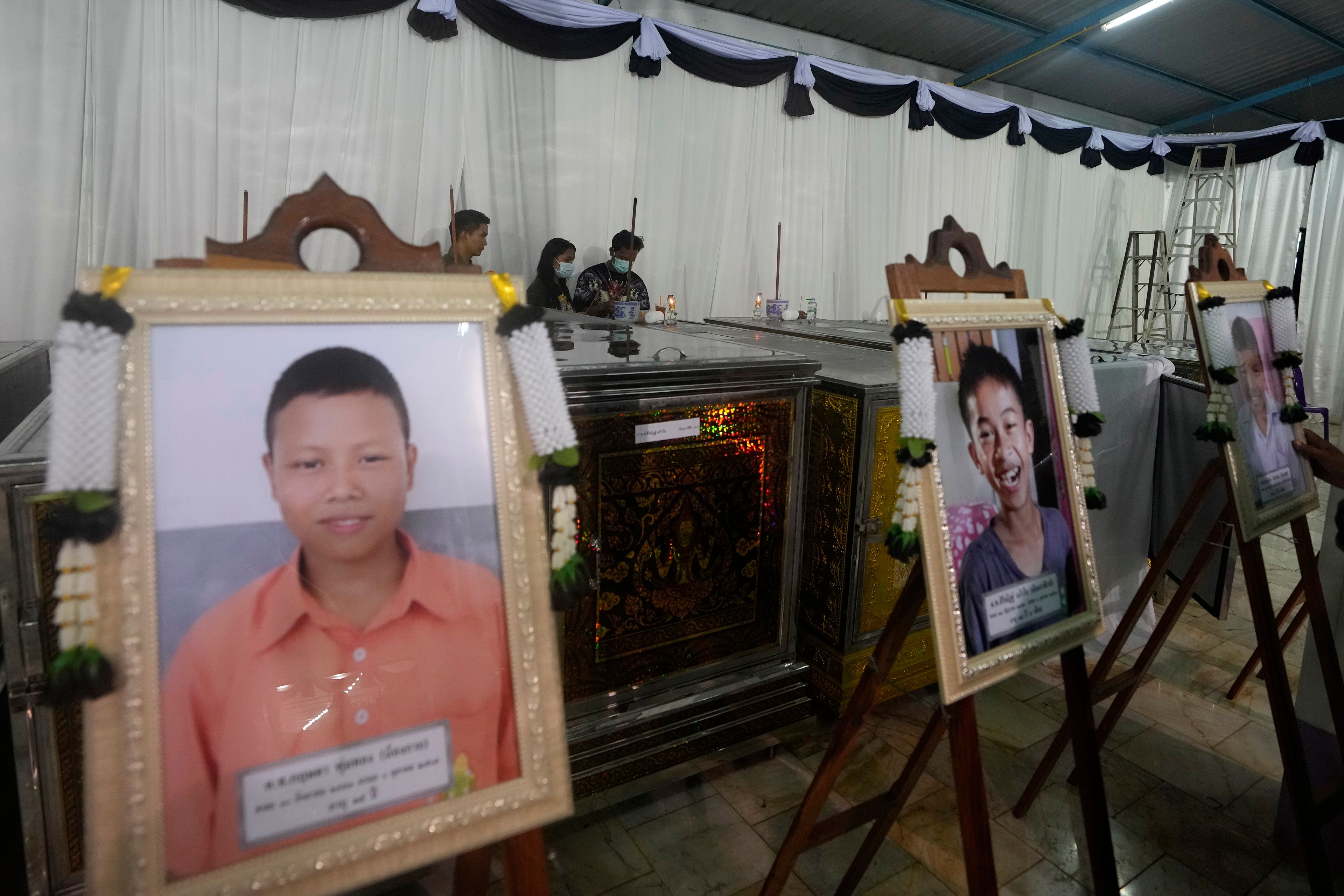 Portraits of the bus fire victims are placed in front of their coffins at the Wat Khao Phraya Sangkharam School Lan Sak, Uthai Thani province, Thailand, Wednesday, Oct. 2, 2024. (AP Photo/Sakchai Lalit)