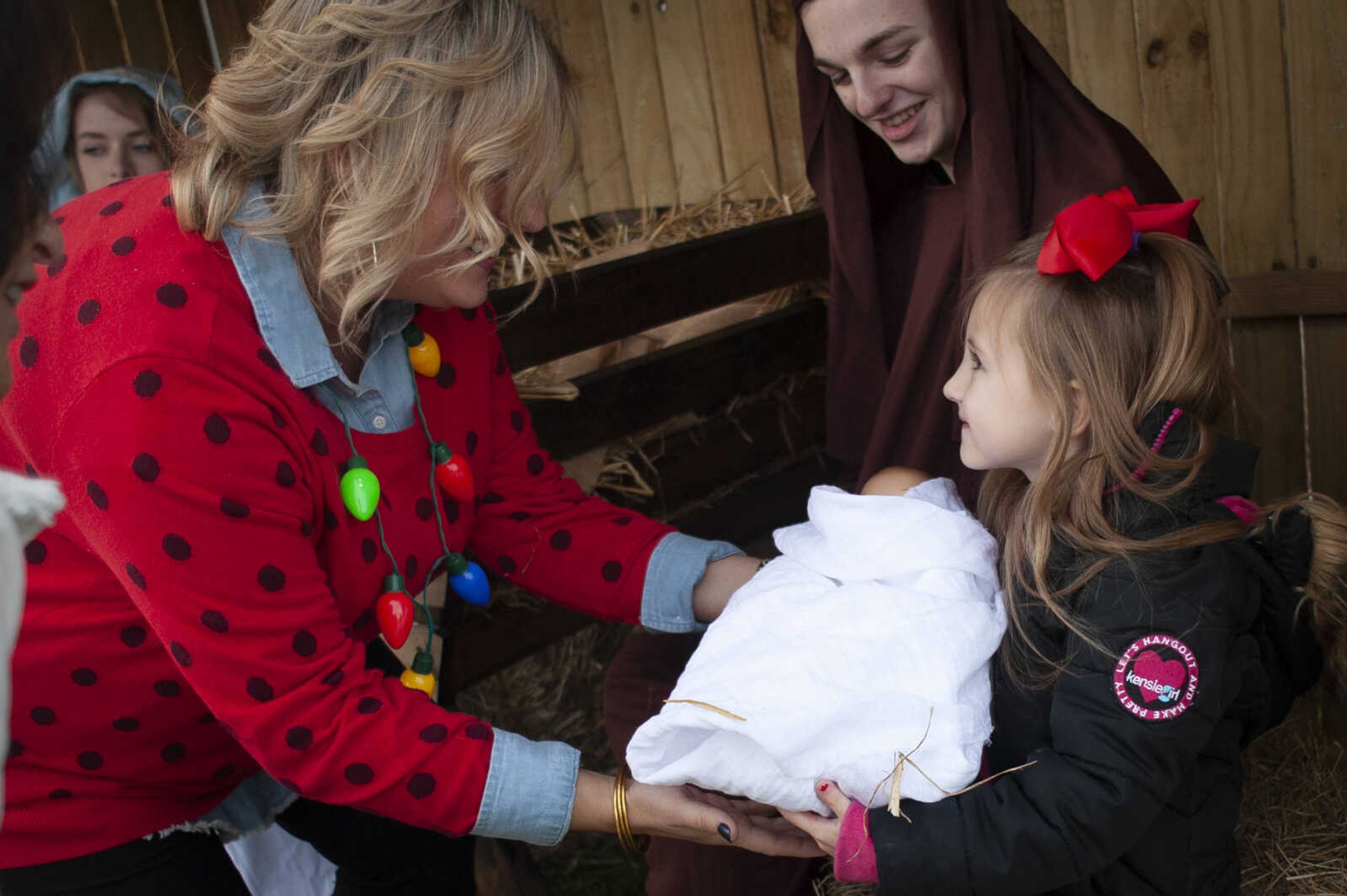 Blakely Phillips, 4, of Jackson holds a baby doll representing Jesus Christ while being assisted by Heather Short, training and development officer at the bank, next to Sam Bonney, 17, of Cape Girardeau, portraying Joseph, during a living nativity Thursday, Dec. 12, 2019, at First Midwest Bank in Cape Girardeau.