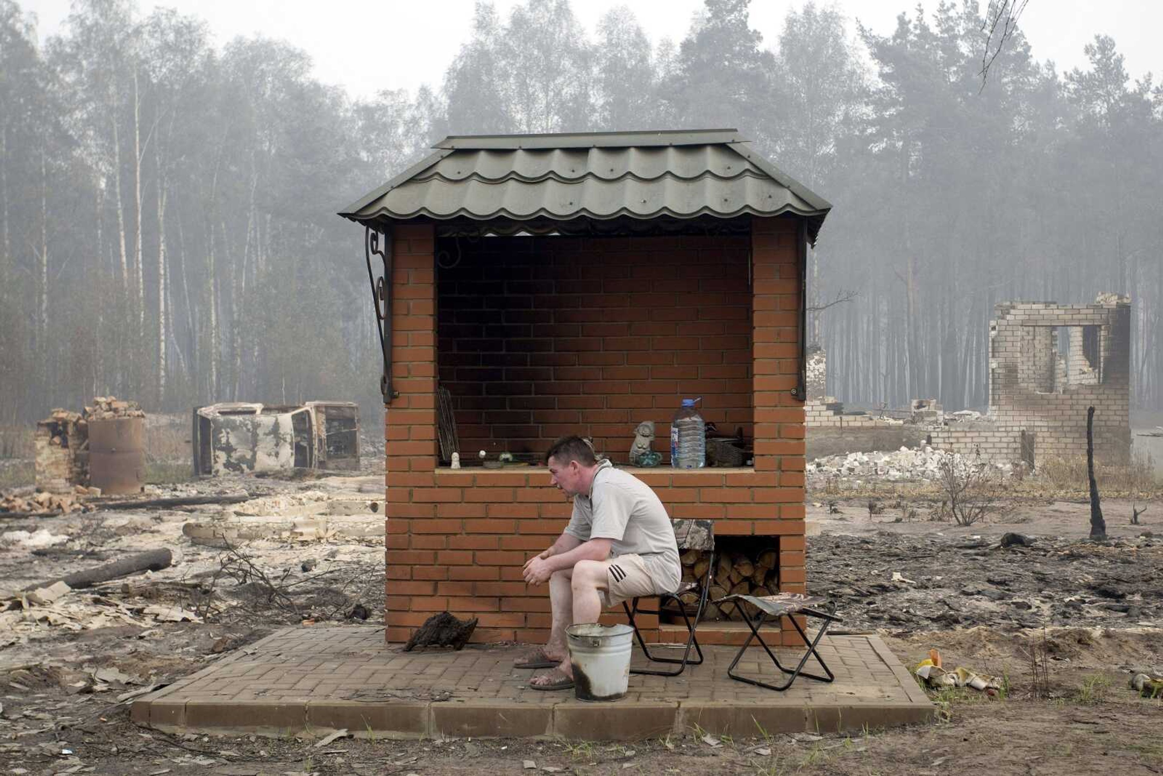 A man sits near his mangal, an outdoor barbecue, Saturday. It was left untouched by a spreading wildfire, which burned his house and a car to the ground, background, as well as the entire village of Peredeltsy in Ryazan region, some 111 miles southeast of Moscow. (Associated Press)