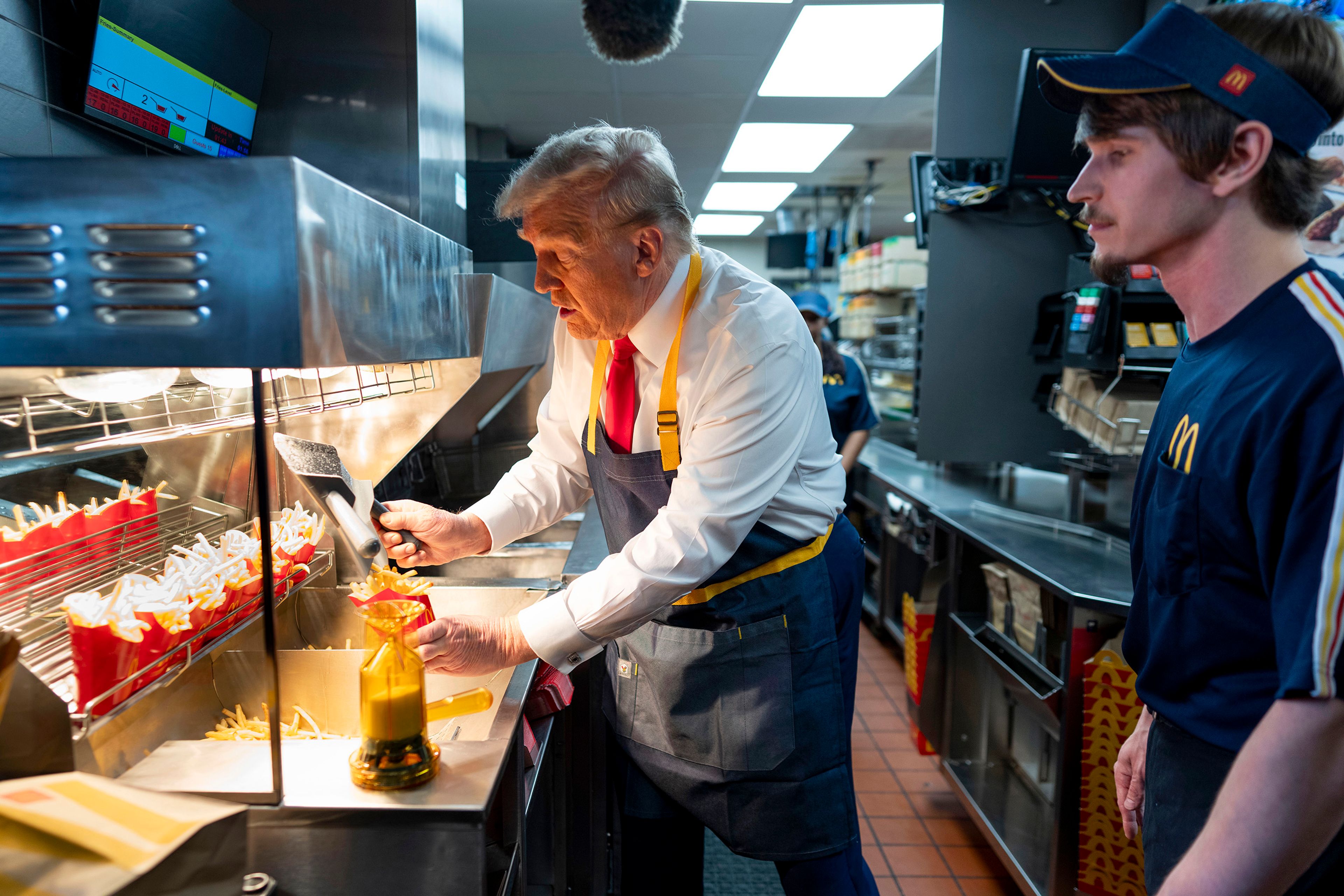 Republican presidential nominee former President Donald Trump, left, uses a frier as an employee looks on during a visit to McDonald's in Feasterville-Trevose, Pa., Sunday, Oct. 20, 2024. 