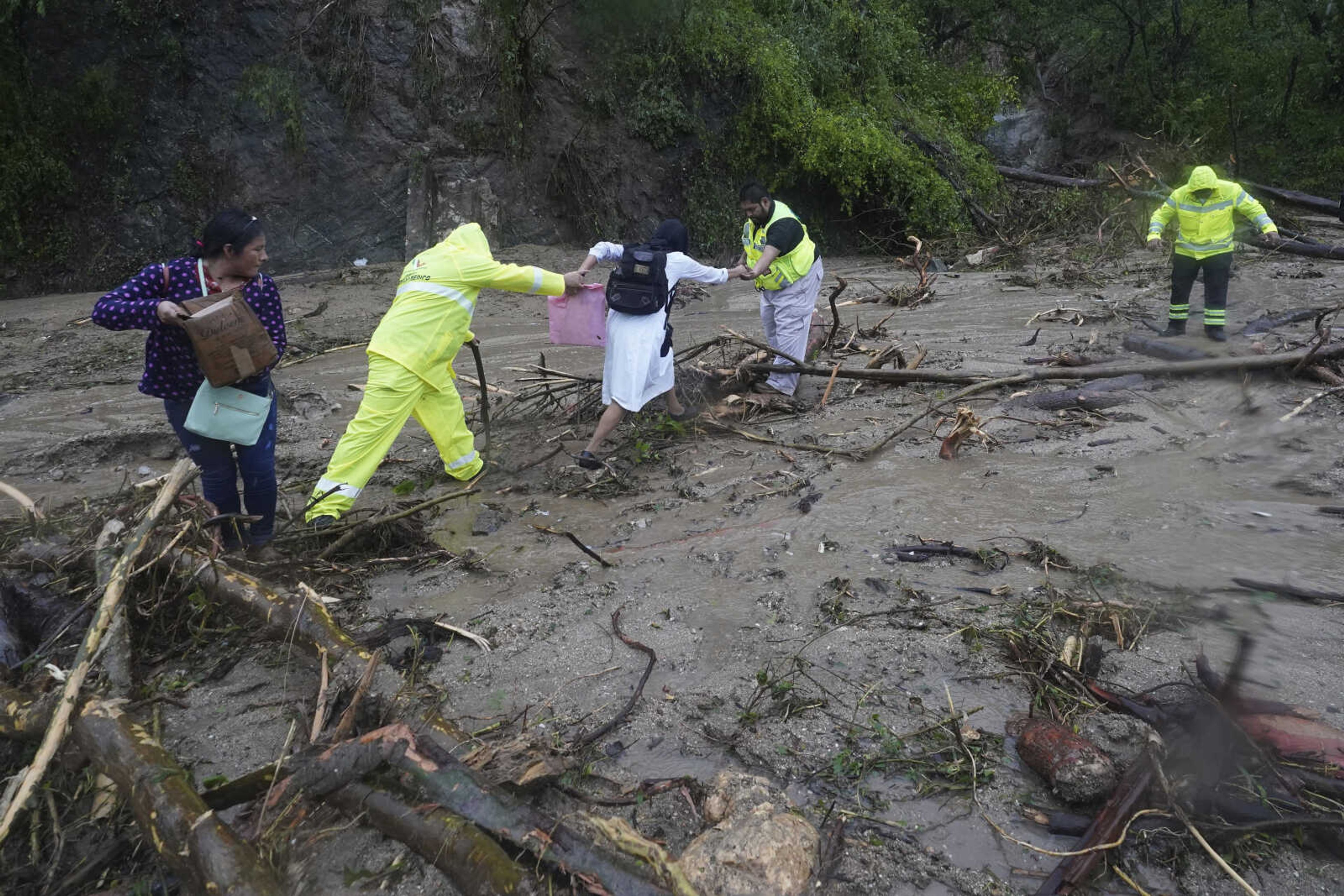 People are helped as they cross a highway blocked by a landslide triggered by Hurricane Otis on Wednesday near Acapulco, Mexico.