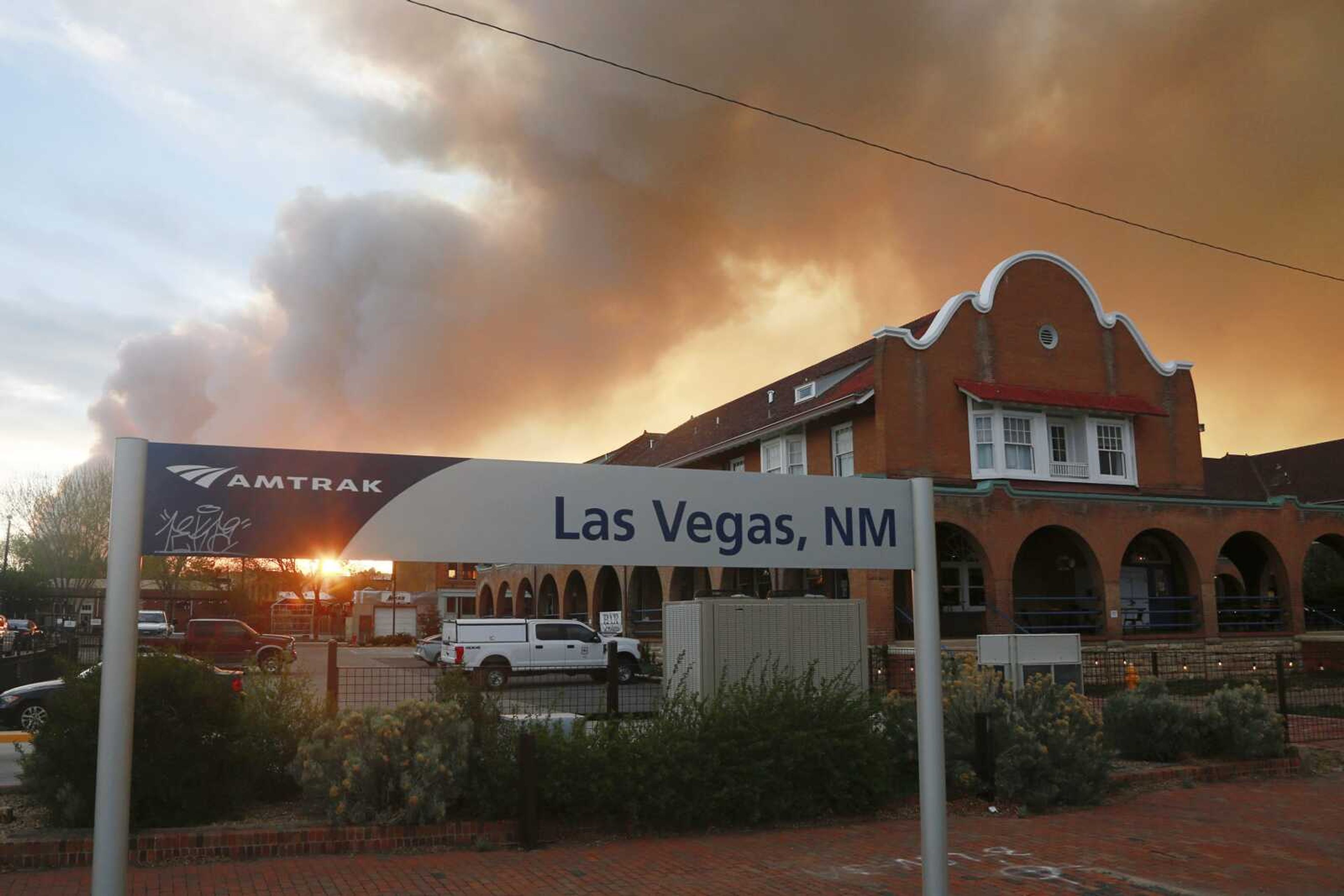 A sunset seen through a wall of wildfire smoke from the Amtrak train station Saturday in Las Vegas, New Mexico. The Castaneda Hotel, right, hosted meals for residents and firefighters last week with sponsorships from restaurants and other businesses.