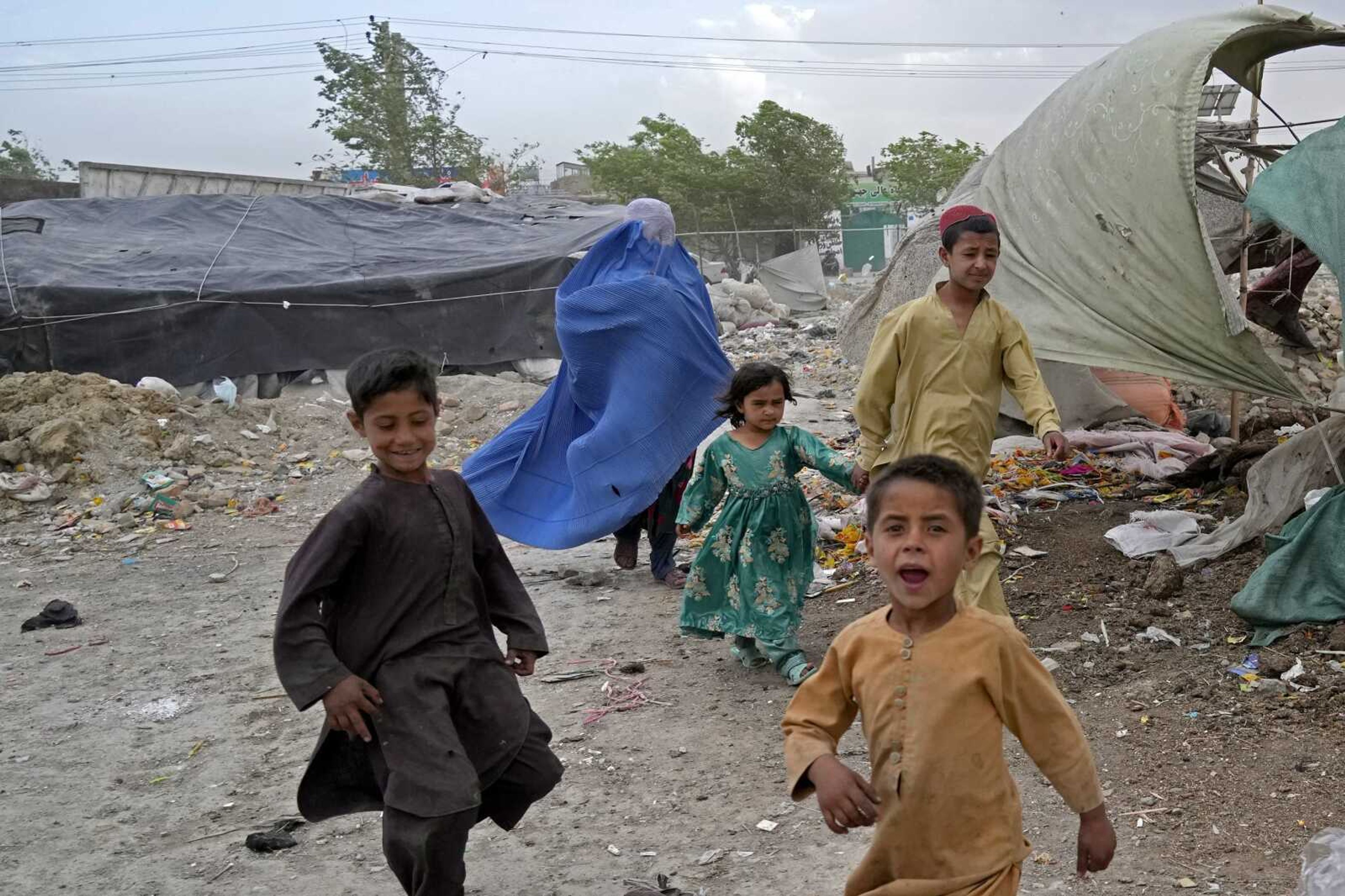 A woman wearing a burqa and her children walk in front of their house Sunday in Kabul, Afghanistan. Afghan women are furious and fearful over a recent decree by the country's Taliban leaders reinstating the burqa and similar outfits as mandatory for them in public. But some are defying the strict interpretation of Islamic dress codes, venturing out with less restrictive versions than that which the Taliban demanded -- outfits that only reveal their eyes.