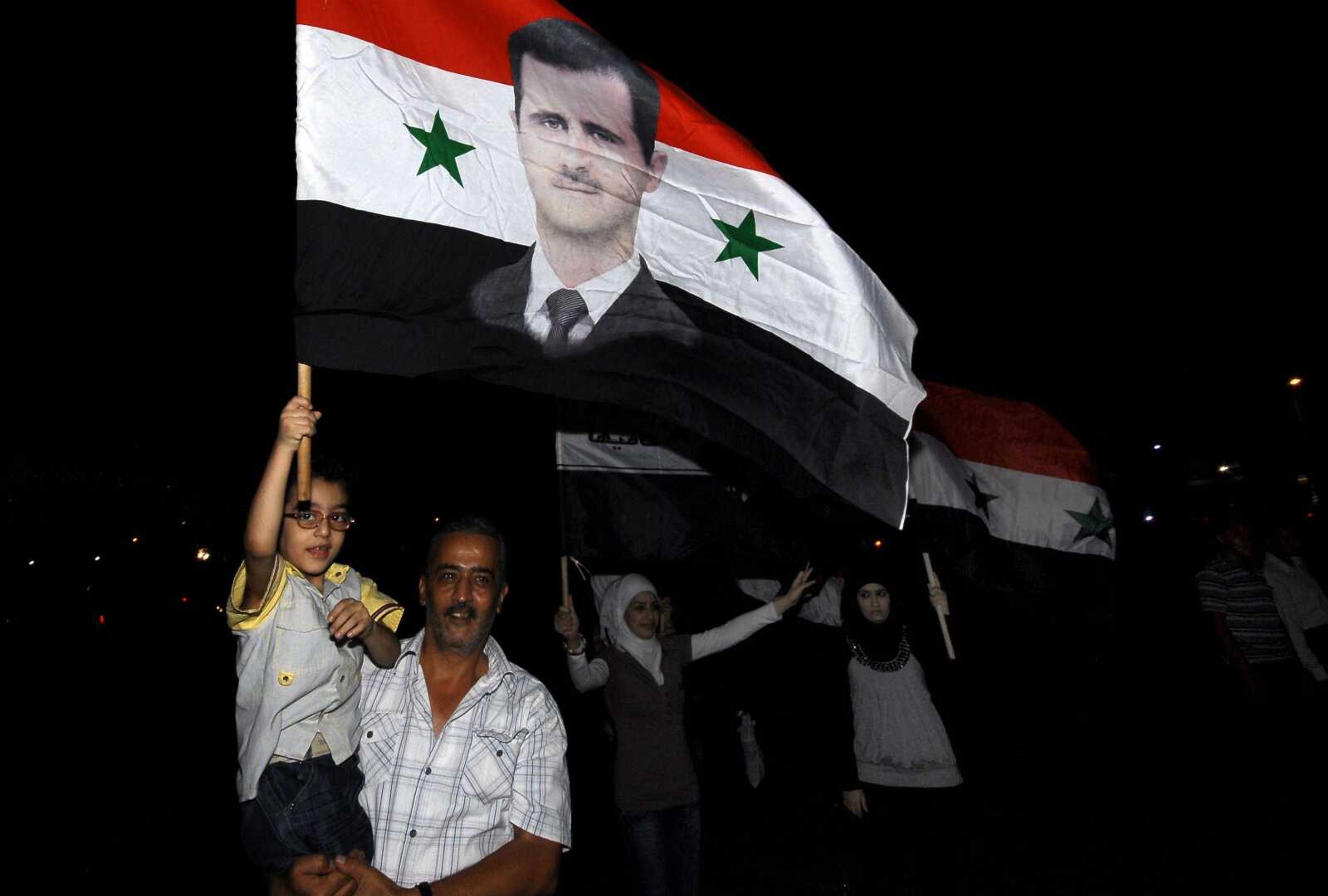 Syrians carry national flags depicting President Bashar Assad, after Assad's interview on state-run TV, in Omawiyeen Square, Damascus, Syria, Sunday, Aug. 21, 2011. Assad said Sunday his regime was in no danger of collapse and warned against any foreign military intervention in his country as the regime tries to crush a 5-month-old popular uprising. (AP Photo/Muzaffar Salman)