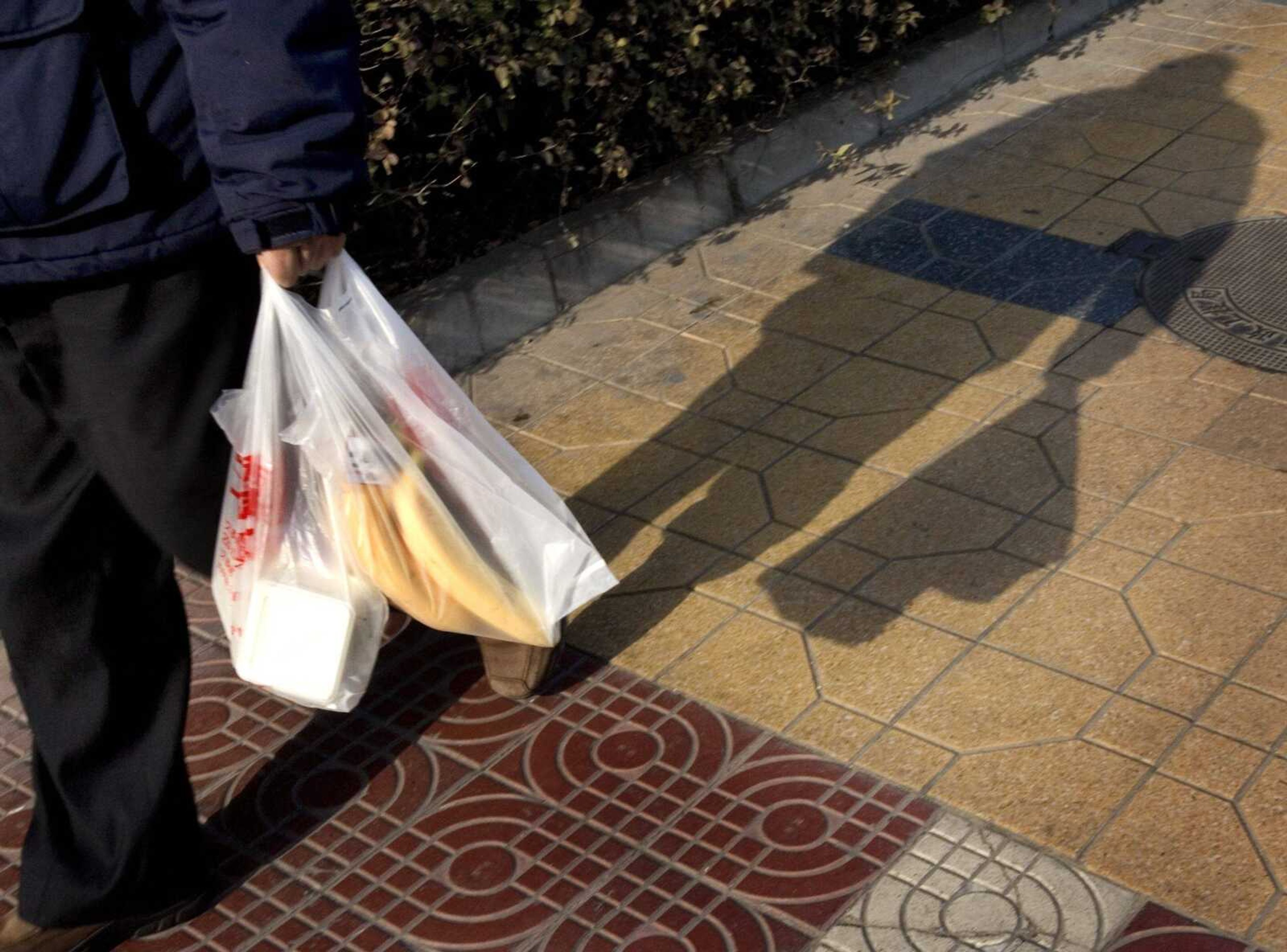 A Chinese man used plastic bags to carry his goods Wednesday in Beijing. China's government announced it will ban shops from giving out free plastic bags and called on consumers to use baskets and cloth sacks instead to reduce environmental pollution. (ANDY WONG ~ Associated Press)