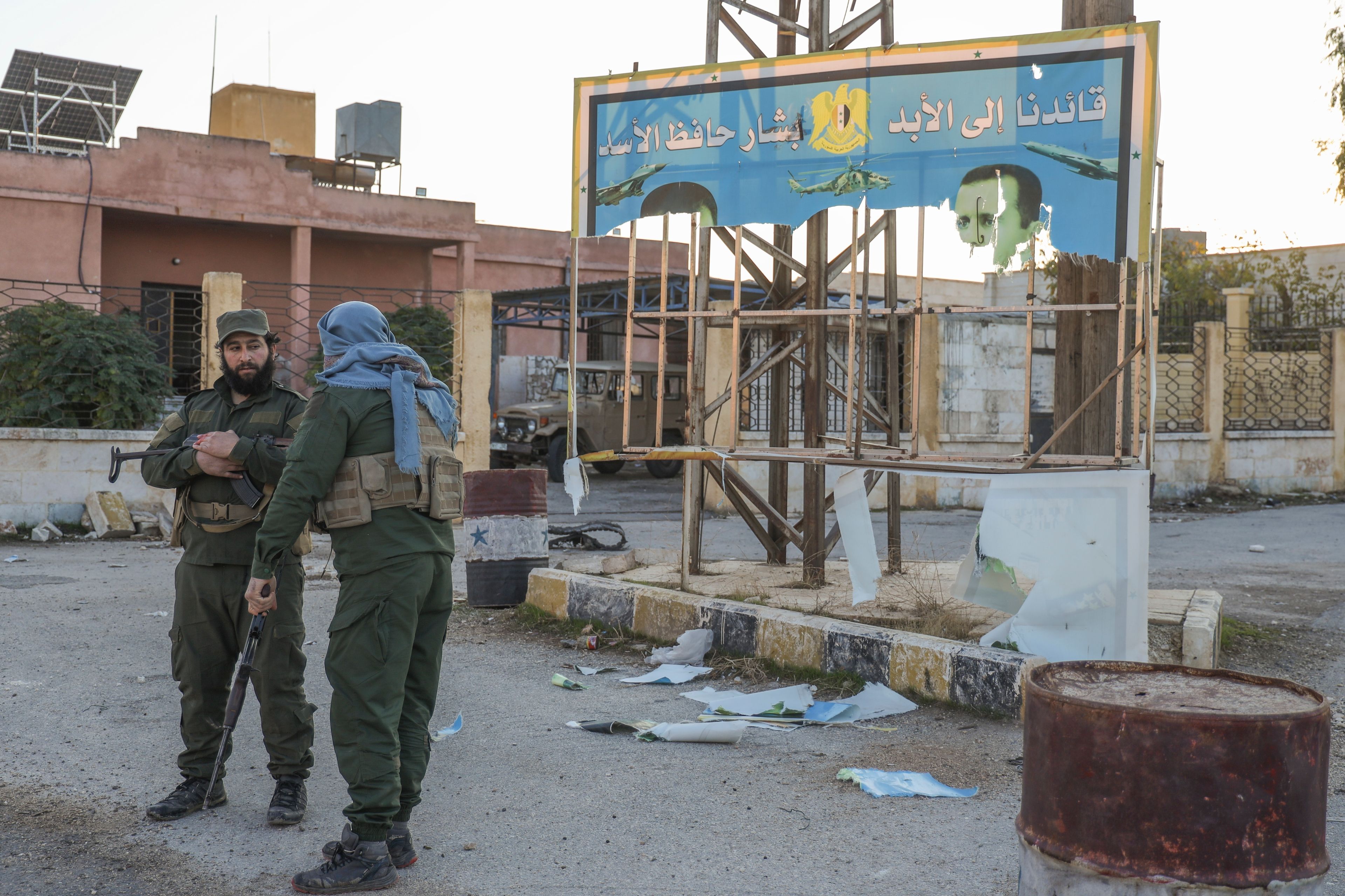 Syrian opposition fighters stand next to a government sign after entering the village of Anjara, western outskirts of Aleppo, Syria, Thursday Nov. 28, 2024, part of their major offensive on government-controlled areas in the country's northwestern Syria. (AP Photo/Omar Albam)