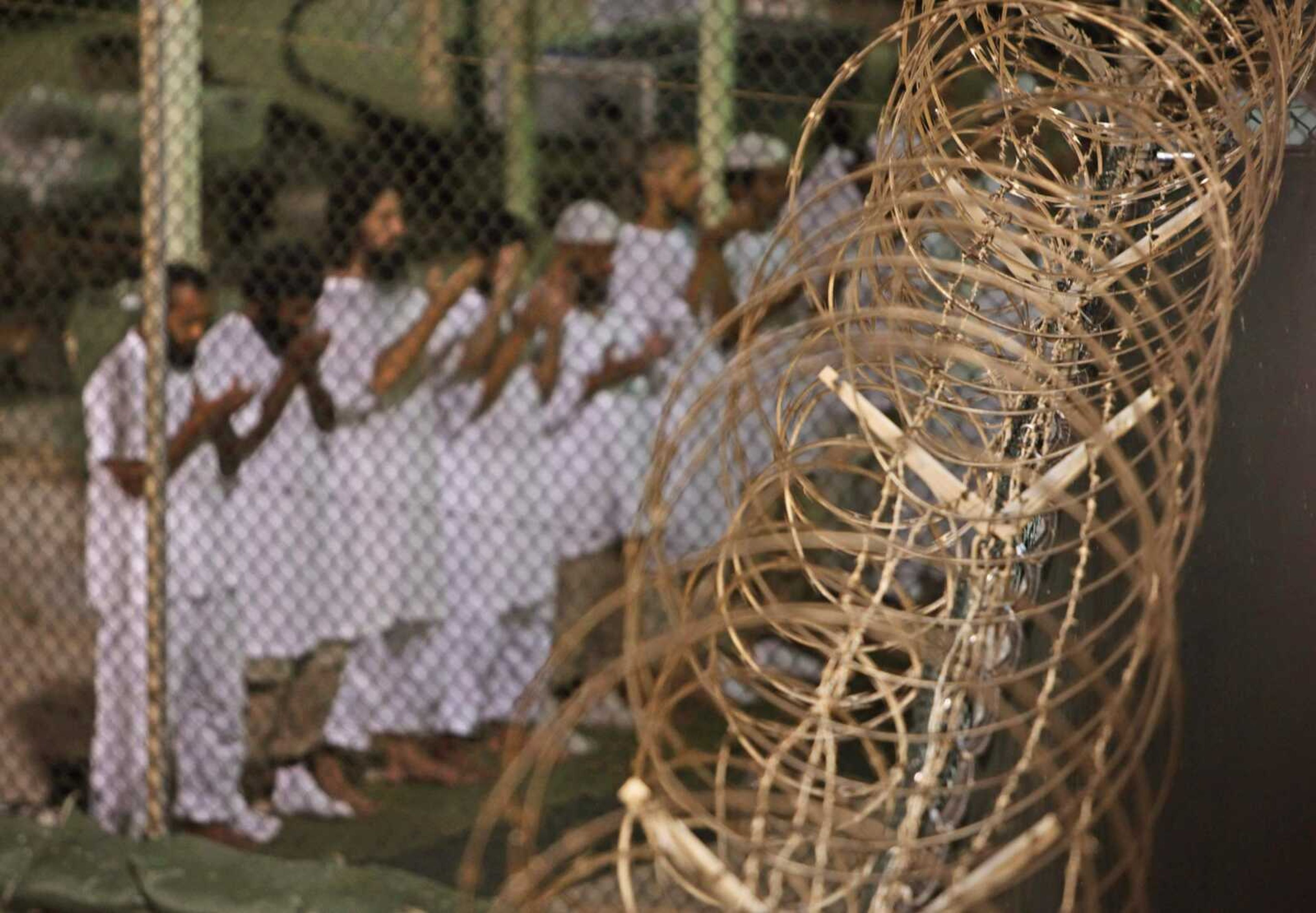 In this May 14, 2009, file photo, reviewed by the U.S. military, Guantanamo detainees pray before dawn near a fence of razor wire inside Camp 4 detention facility at Guantanamo Bay U.S. Naval Base, Cuba. (Brennan Linsley ~ Associated Press)