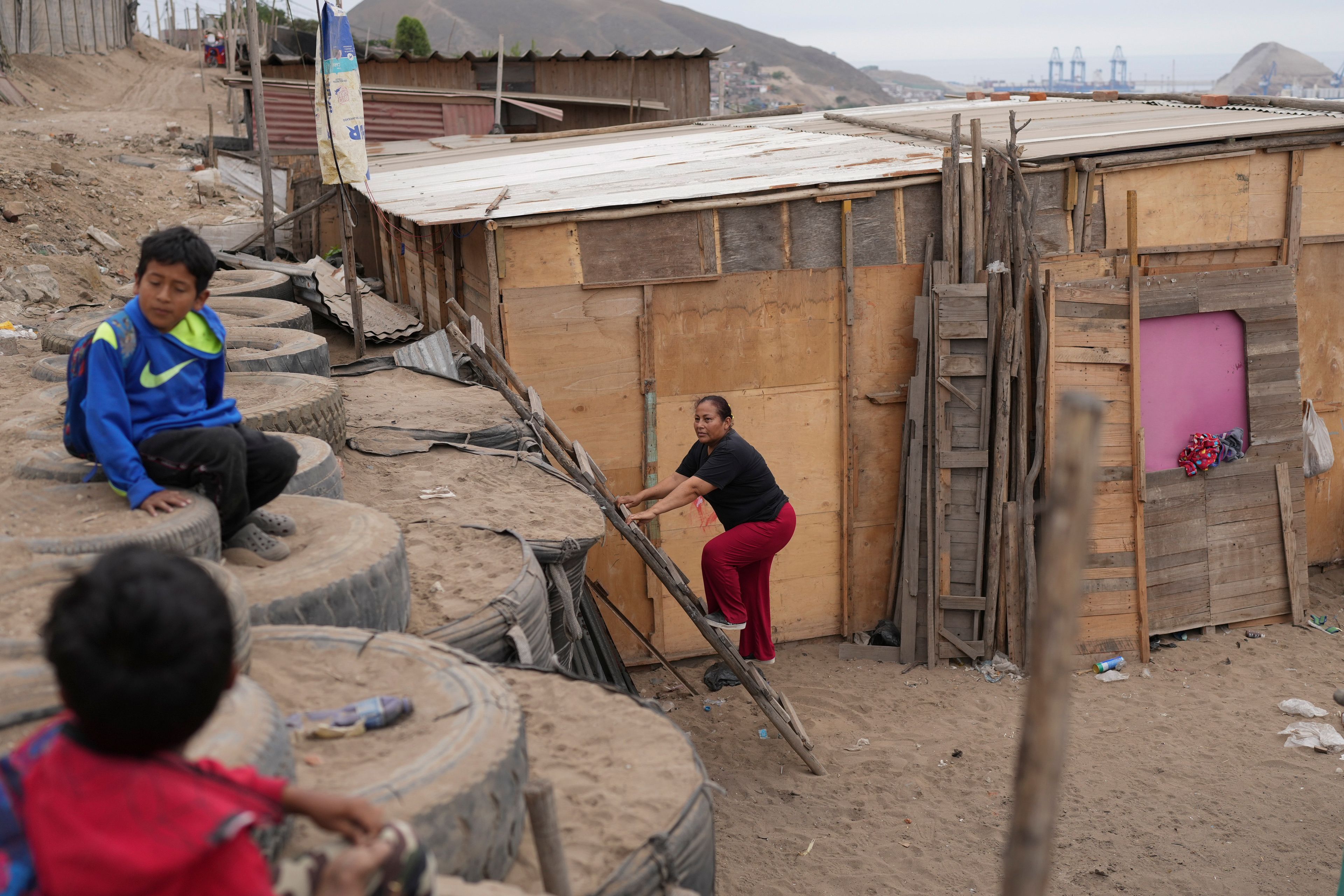 Nelly Lopez climbs up a ladder to leave her home in the Senor de la Soledad shantytown near a Chinese-funded port construction in Chancay, Peru, Tuesday, Nov. 12, 2024. (AP Photo/Silvia Izquierdo)