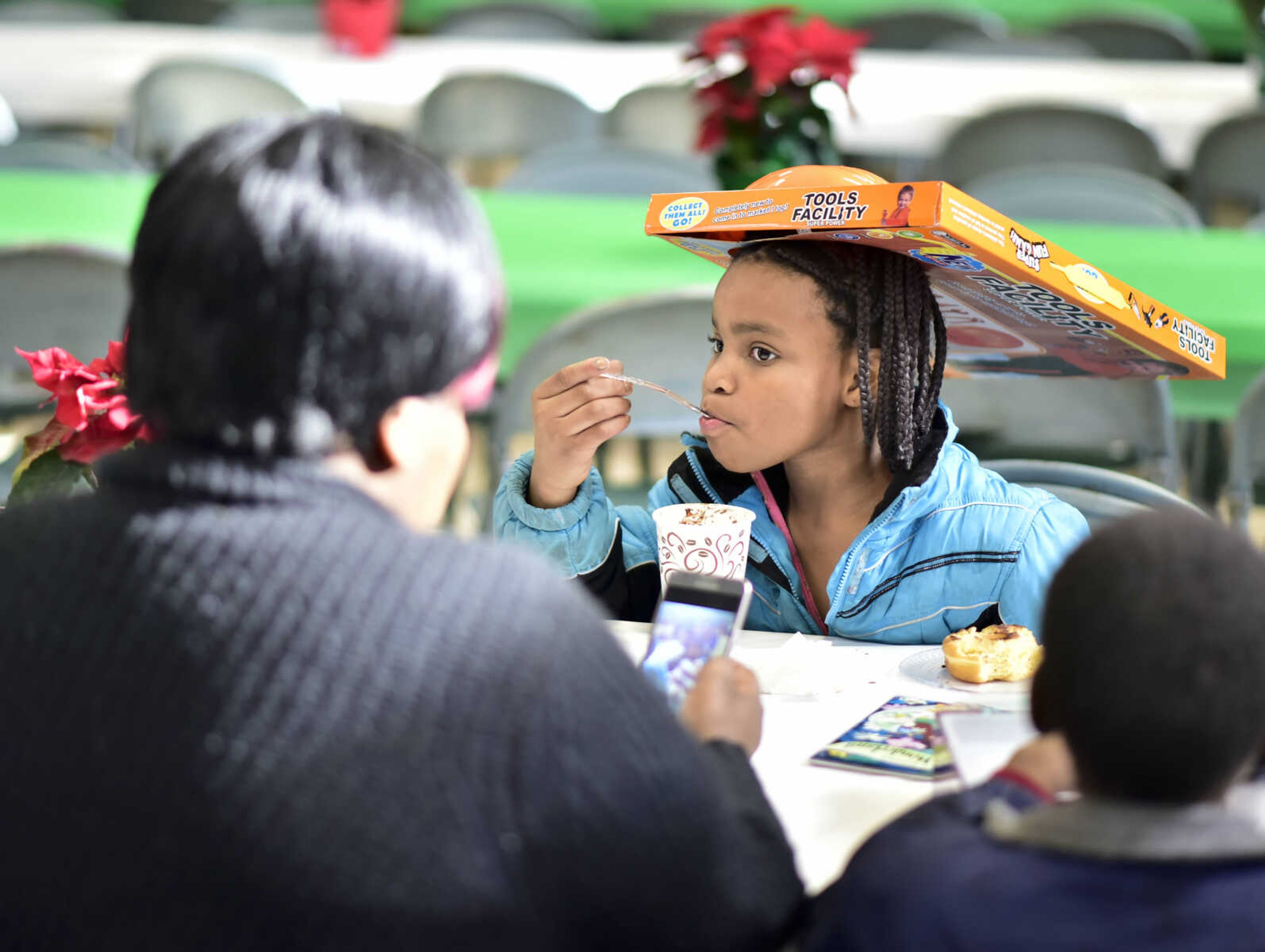 Jessica Gilbert, 9, takes a bite while wearing her brother's present on her head during a free lunch hosted by Student Santas on Dec. 25, 2017, at Jefferson Elementary School in Cape Girardeau.