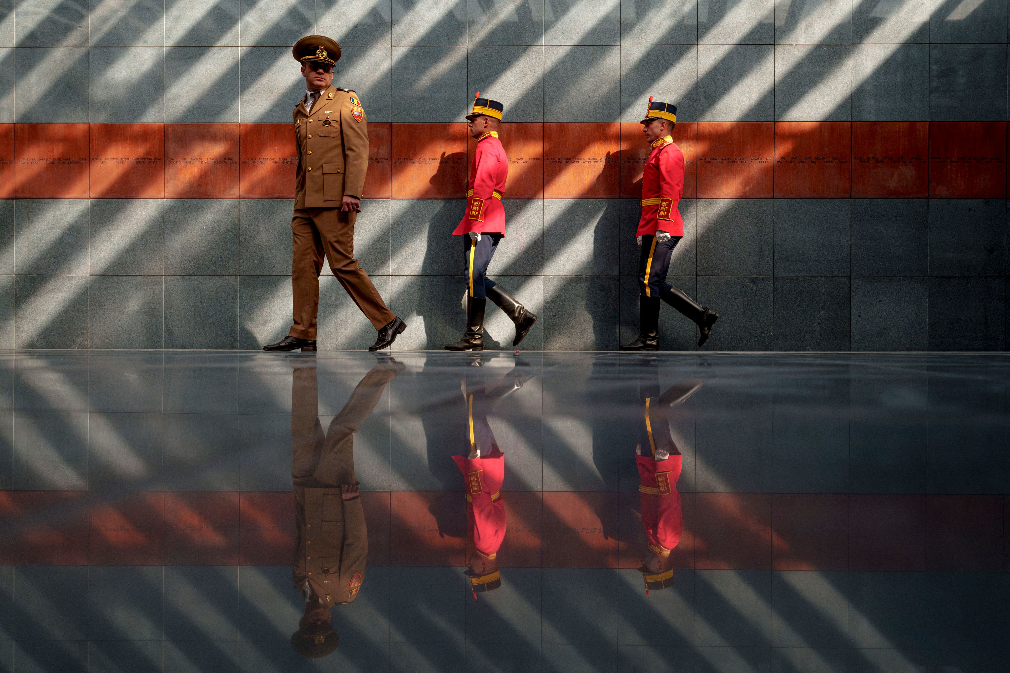 Romanian serviceman walk after laying flower wreaths inside the Holocaust memorial, backdropped by names of victims engraved in rusty metal plates, during the National Holocaust Remembrance Day commemorations in Bucharest, Romania, Wednesday, Oct. 9, 2024, the date when, in 1941, the deportations of Jews and Roma began in the country. (AP Photo/Andreea Alexandru)