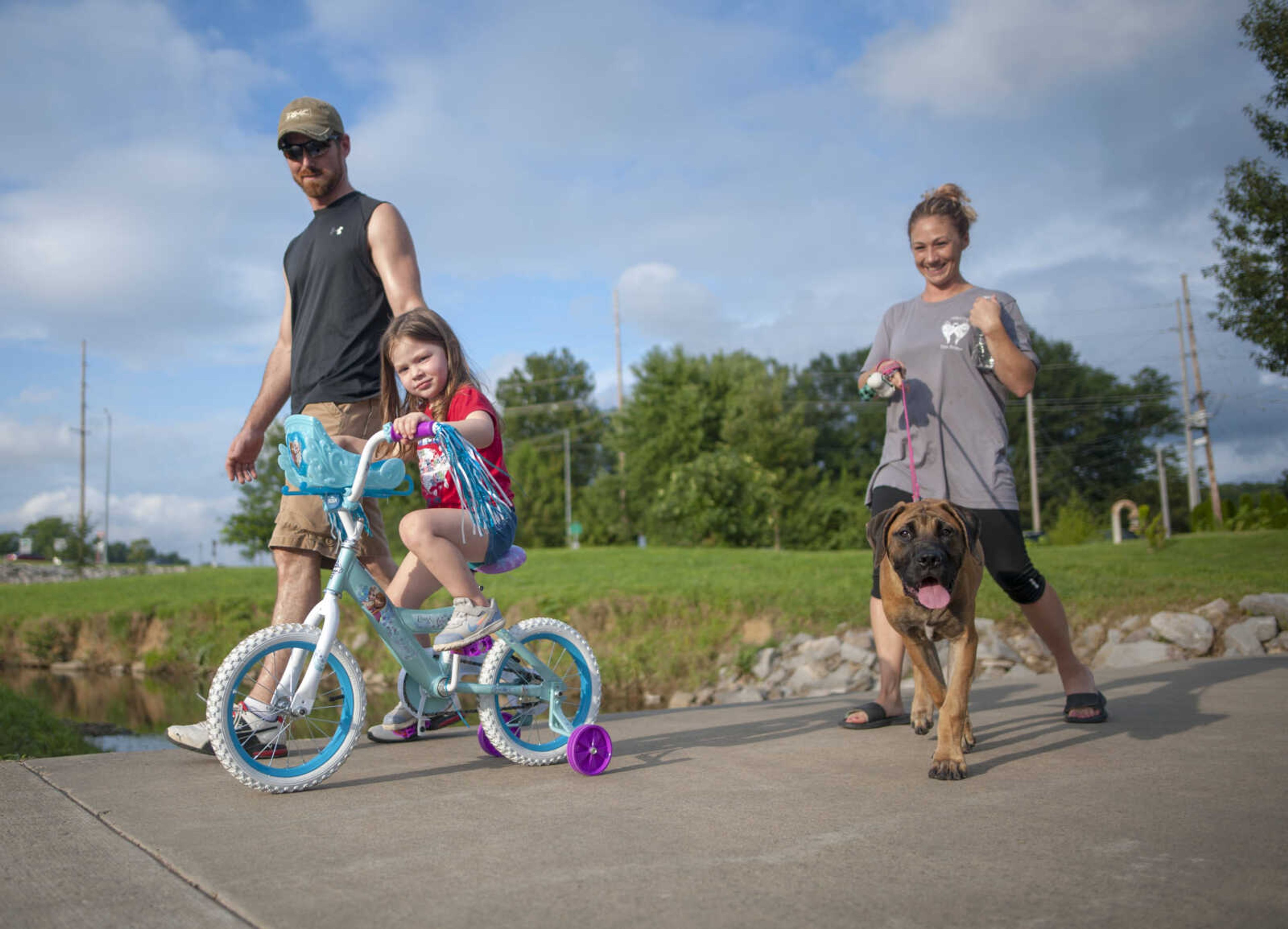 Joined by Cara VanGennip and her 4-month-old puppy Sienna, Neil Briner watches his daughter, Cora, 3, ride her bicycle on her birthday Sunday, Aug. 25, 2019, at the LaCroix Recreation Trail in Cape Girardeau. 