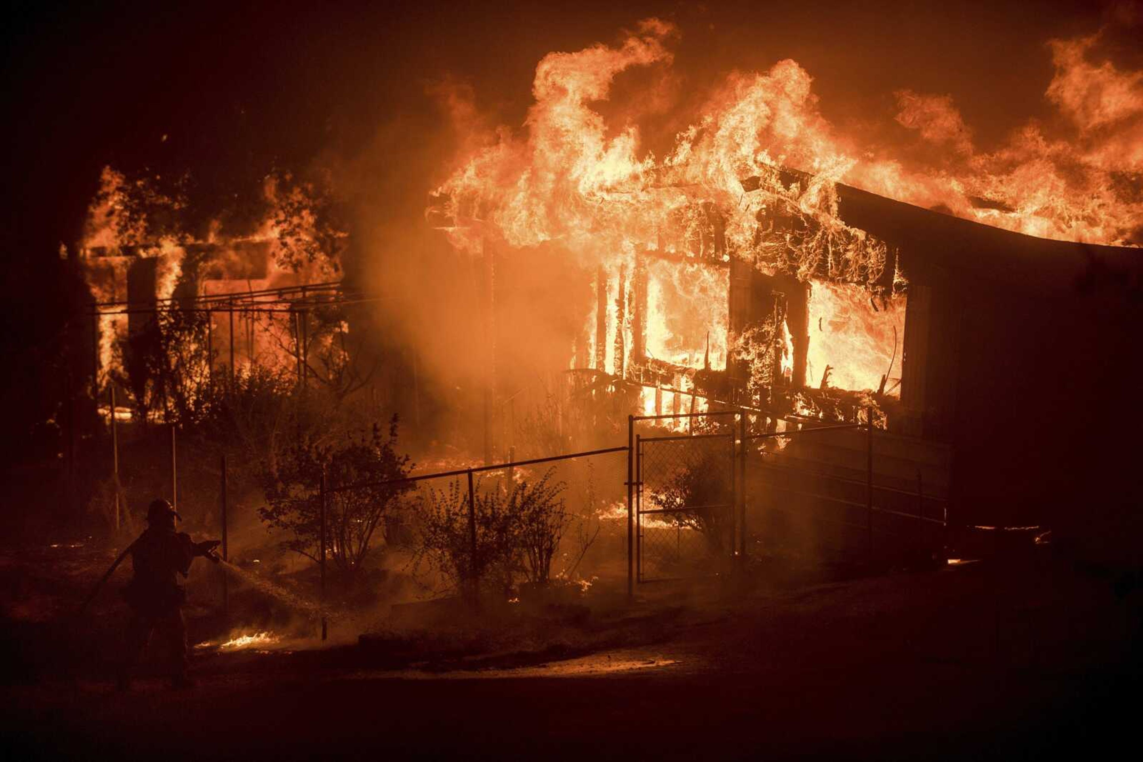 A firefighter sprays water as flames from a wildfire Sunday consume a residence near Oroville, California.