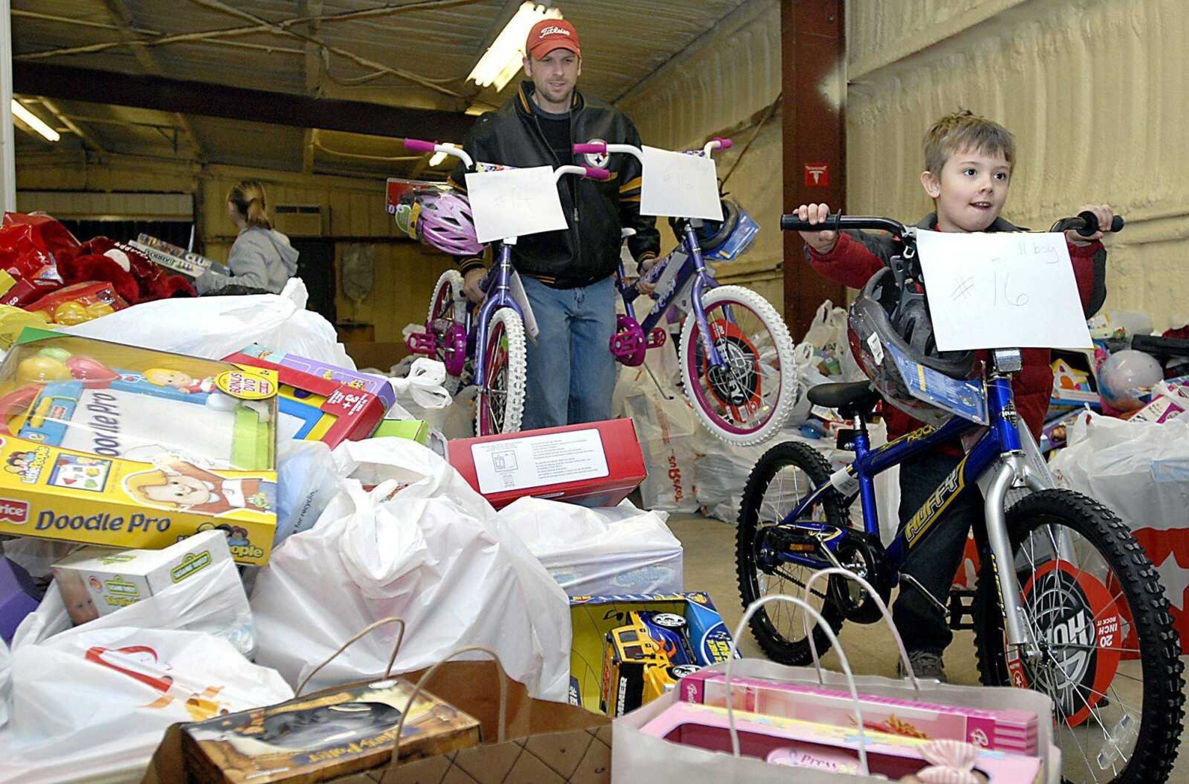 Ron MacCubbin, left, and his son, Clatyon, 4, weaved through toys while transporting bikes to a separate area for sorted gifts with the Jaycees Toybox Tuesday evening. (Kit Doyle)