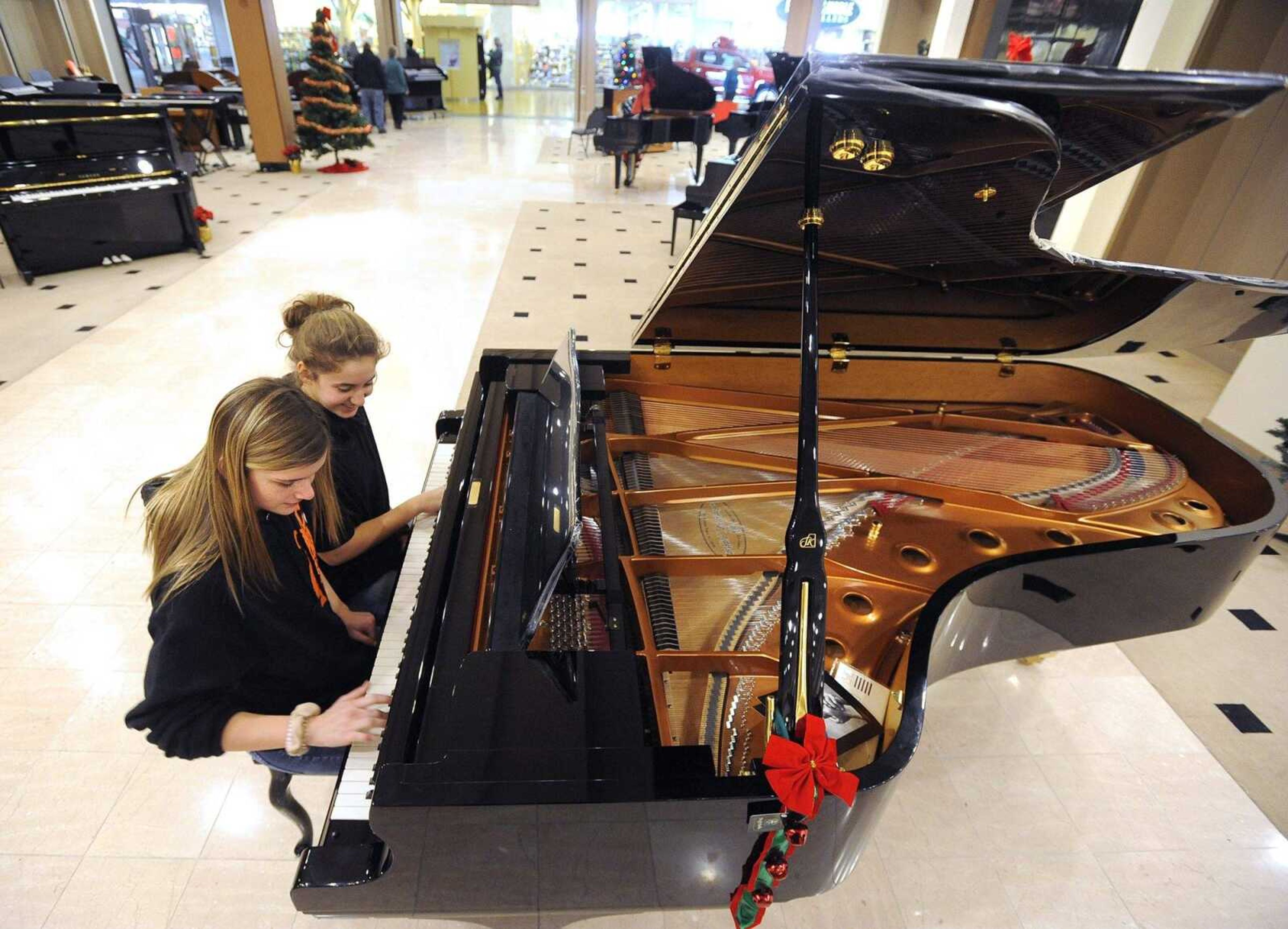 Kiana Newkirk, left, and Lana Woolard try out a Shigeru Kawai grand piano Friday at Lacefield Music in West Park Mall.