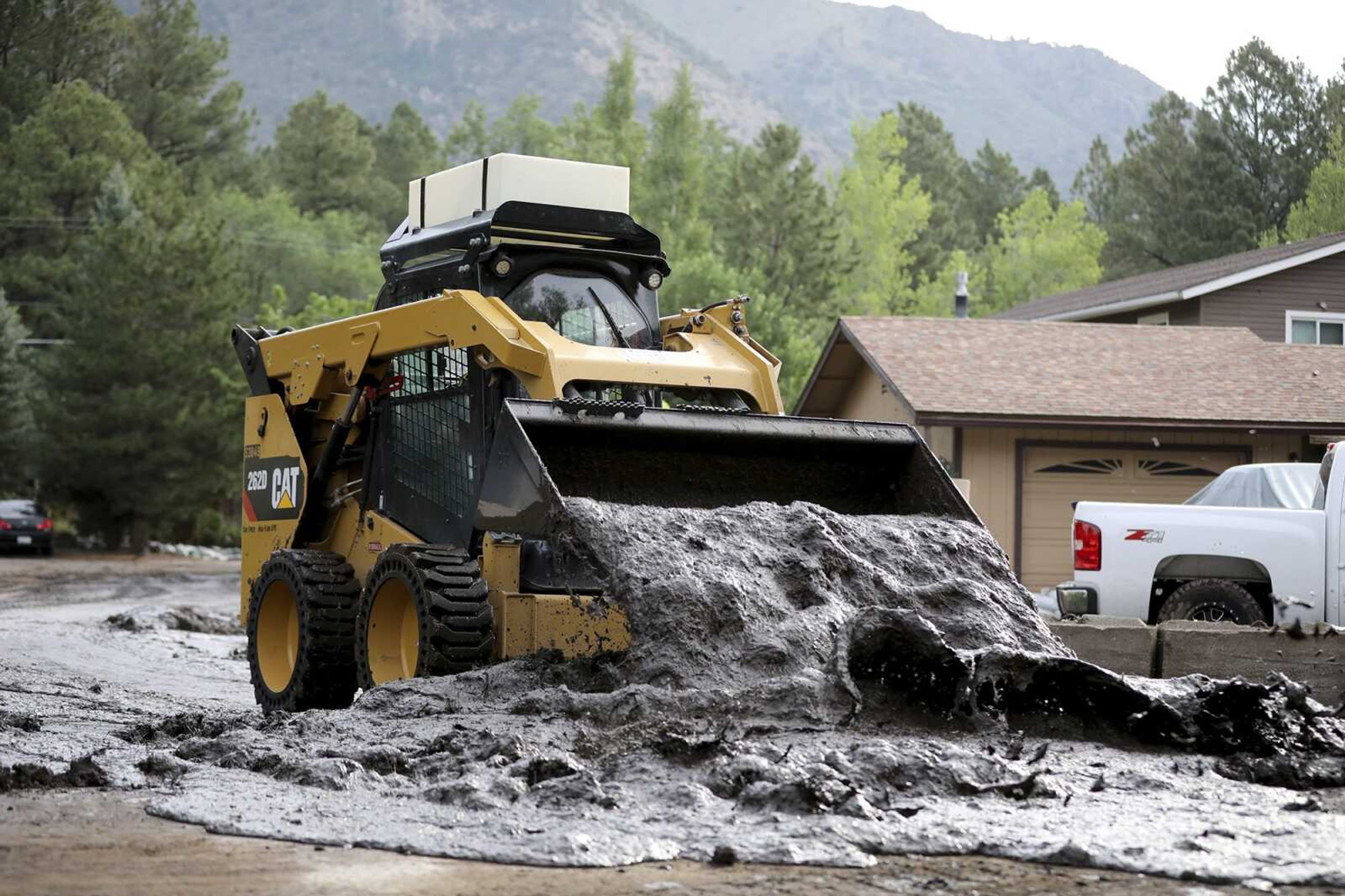 A bobcat moves a wet slurry of ash, mud and forest debris into a pile to be removed after the muck was left behind from flooding caused by a monsoon rain event over the 2019 Museum Fire burn area Wednesday in Flagstaff, Arizona.