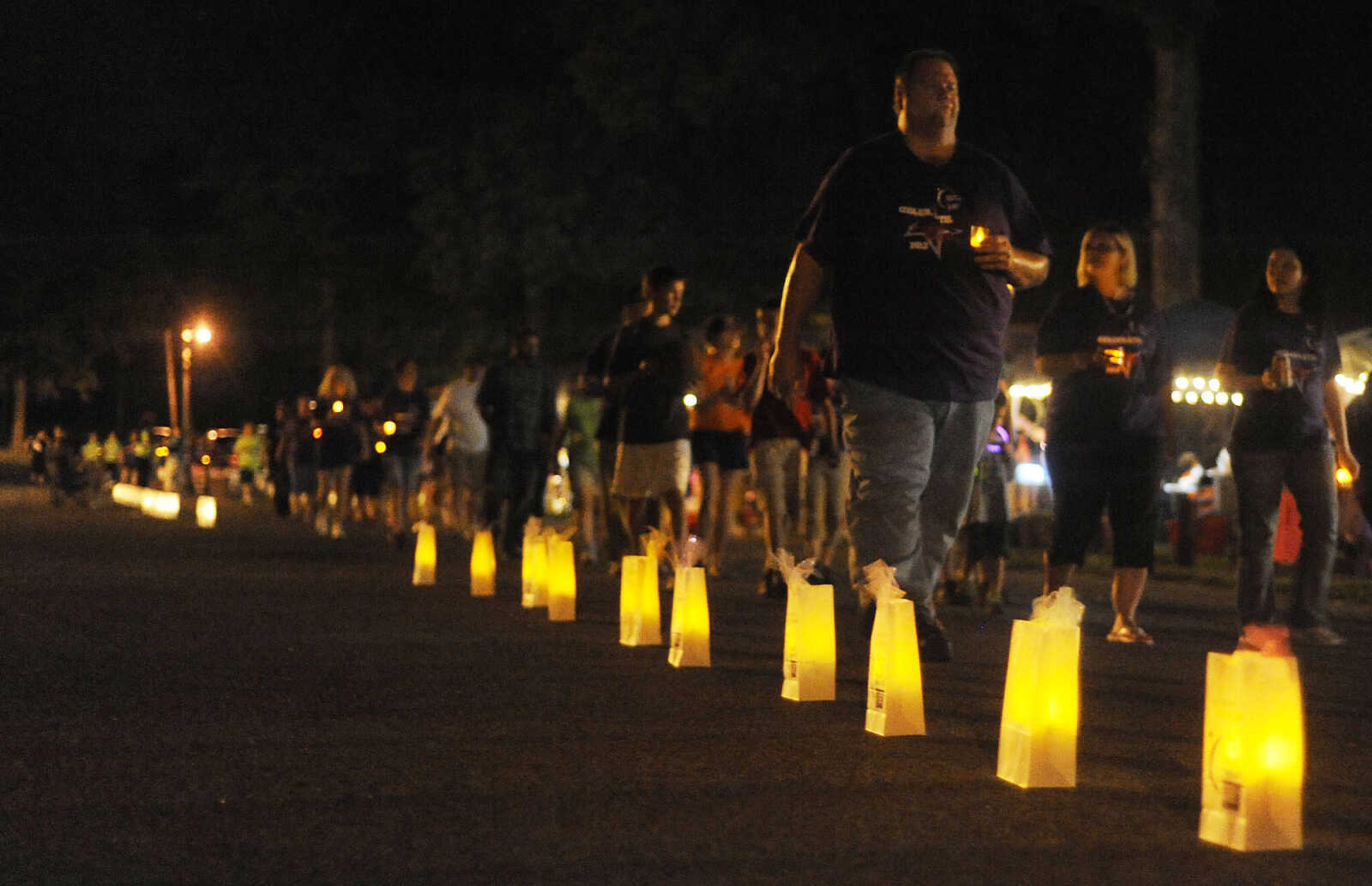 Participants walk past luminaries, paper bags in honor of a cancer survivor or remembrance of friends or family, during the Relay for Life of Cape Girardeau County, Friday, June 14, at Arena Park in Cape Girardeau. This is the 15th year for the event, which serves to raise awareness about cancer while also serving as a fundraiser for the American Cancer Society. Participants form teams which raise money before and during the event.