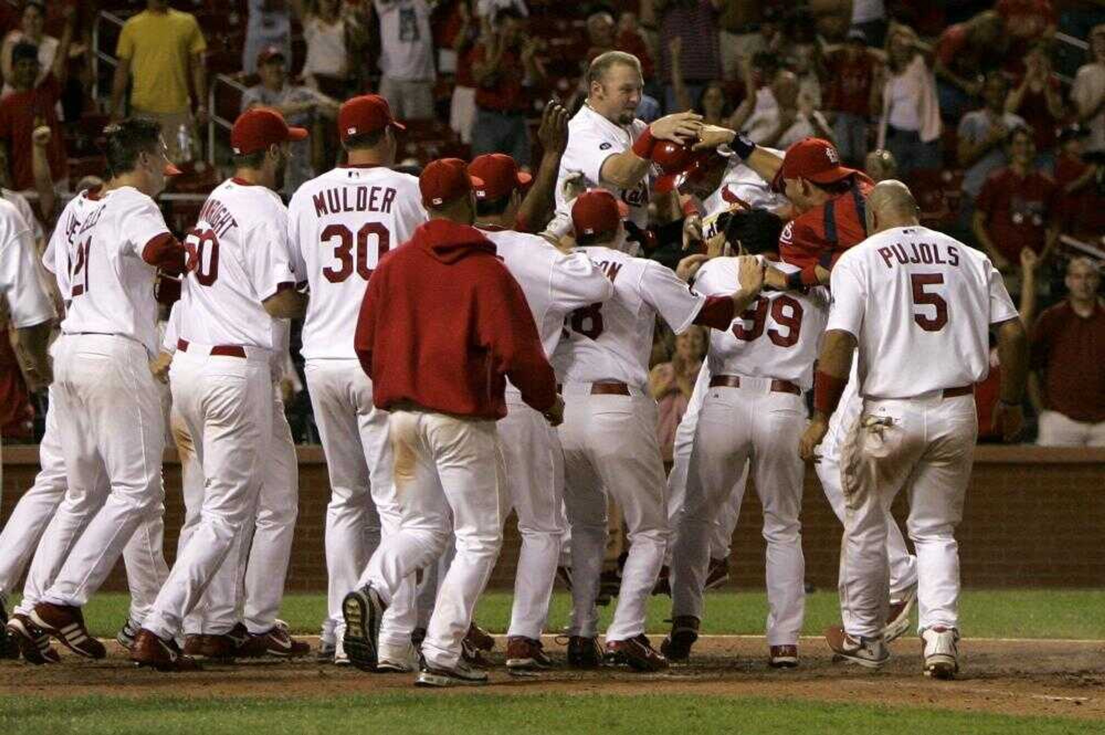 Members of the St. Louis Cardinals gathered around teammate Ryan Ludwick as he landed on home plate for the winning run during the 14th inning early today in St. Louis. Ludwick hit a solo home run to give the Cardinals a 7-6 victory. (Jeff Roberson ~ Associated Press)