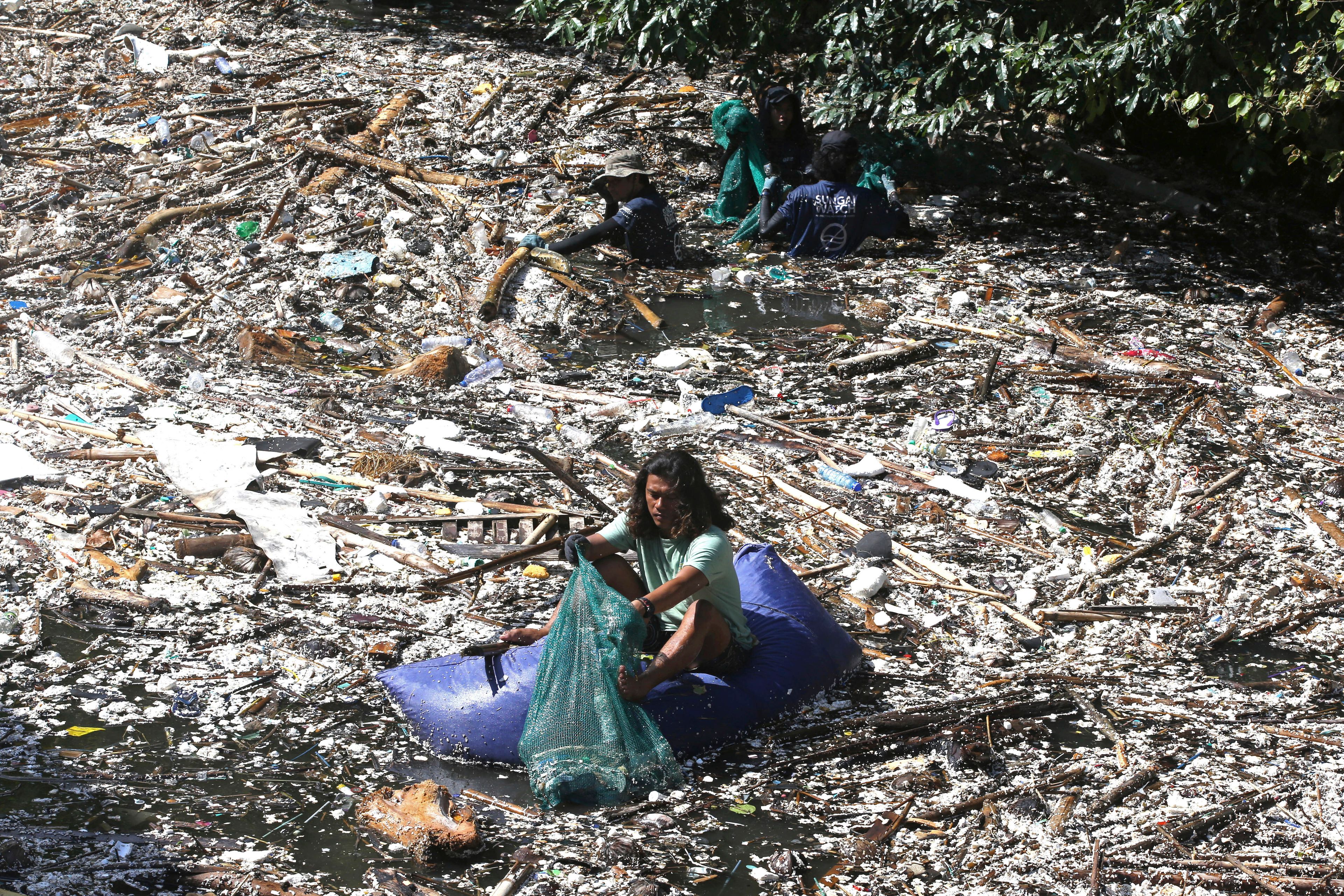 FILE - A volunteer picks up trash on a river which is covered with trash at Pecatu, Bali, Indonesia, March 22, 2024. (AP Photo/Firdia Lisnawati, File)