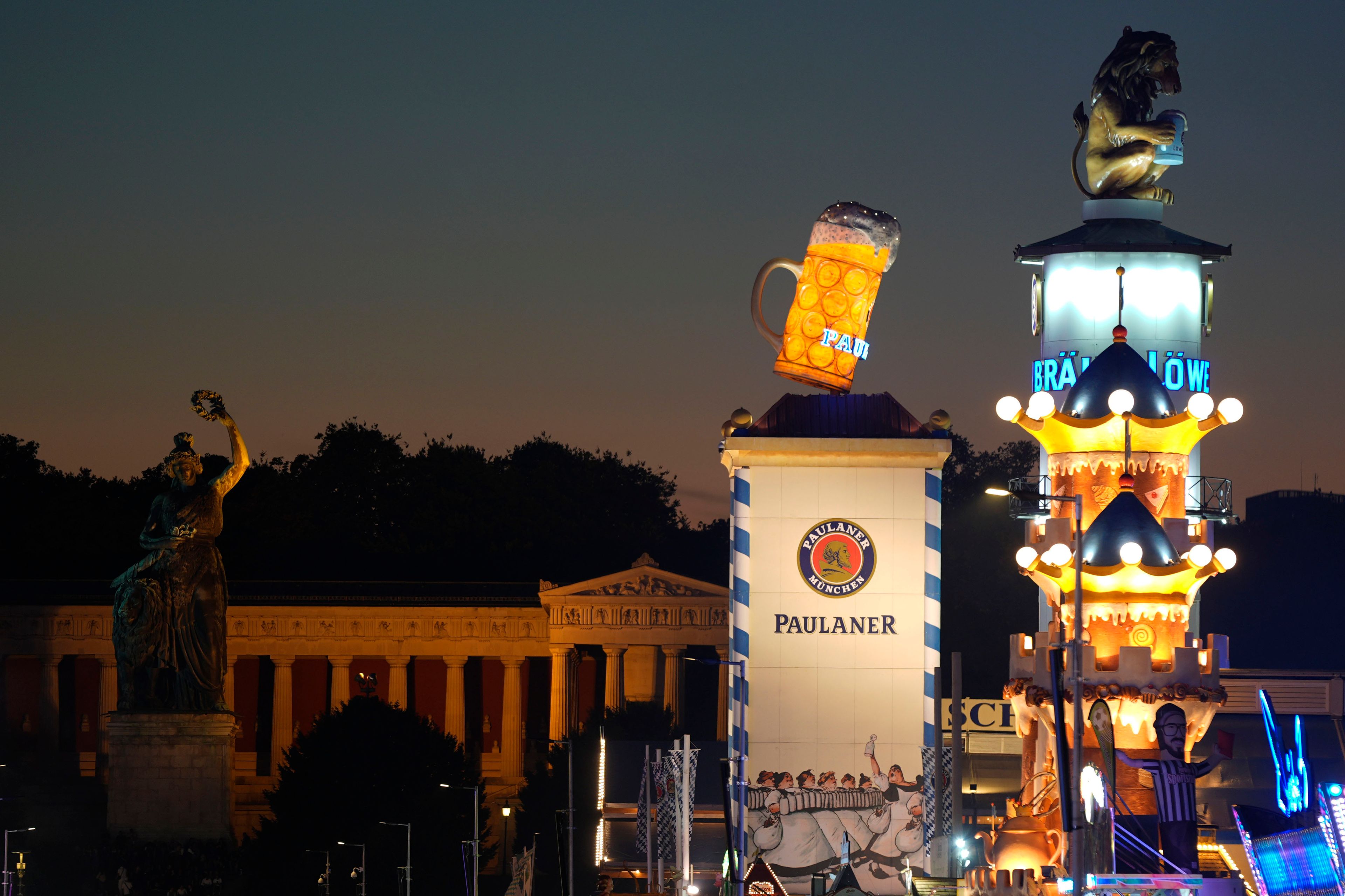 A drinking Lion, the mascot of 'Loewenbraeu' brewery, sits on the rooftop besides a giant beer mug, the logo of 'Paulaner' brewery, on the opening day of the 189th 'Oktoberfest' beer festival in Munich, Germany, Saturday, Sept. 21, 2024. (AP Photo/Matthias Schrader)