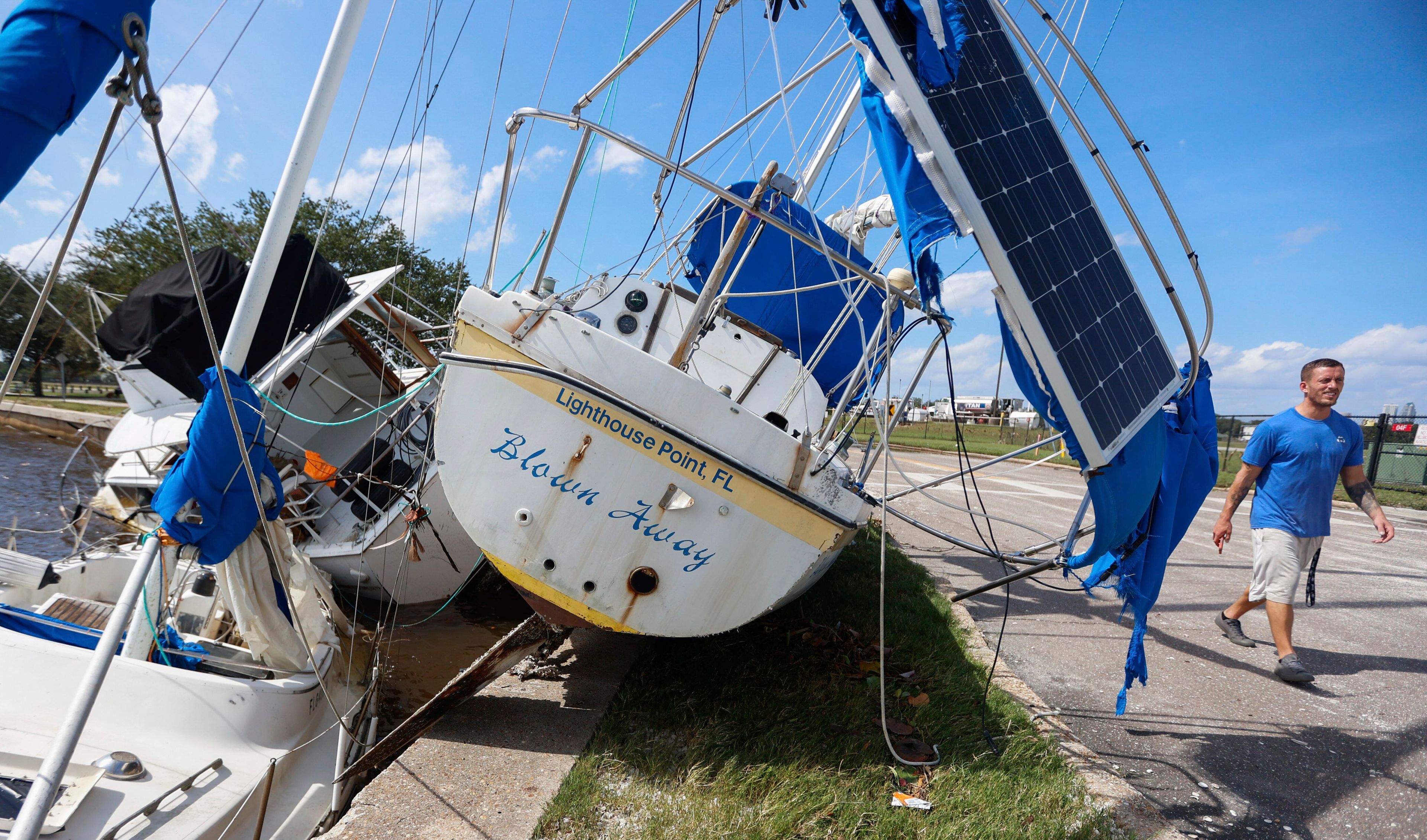 Drew Griffith walks past three boats that washed up against the seawall in the aftermath of Hurricane Helene at the Davis Islands' Seaplane Basin near Peter O. Airport Friday, Sept. 27, 2024 in Tampa, Fla. (Chris Urso/Tampa Bay Times via AP)