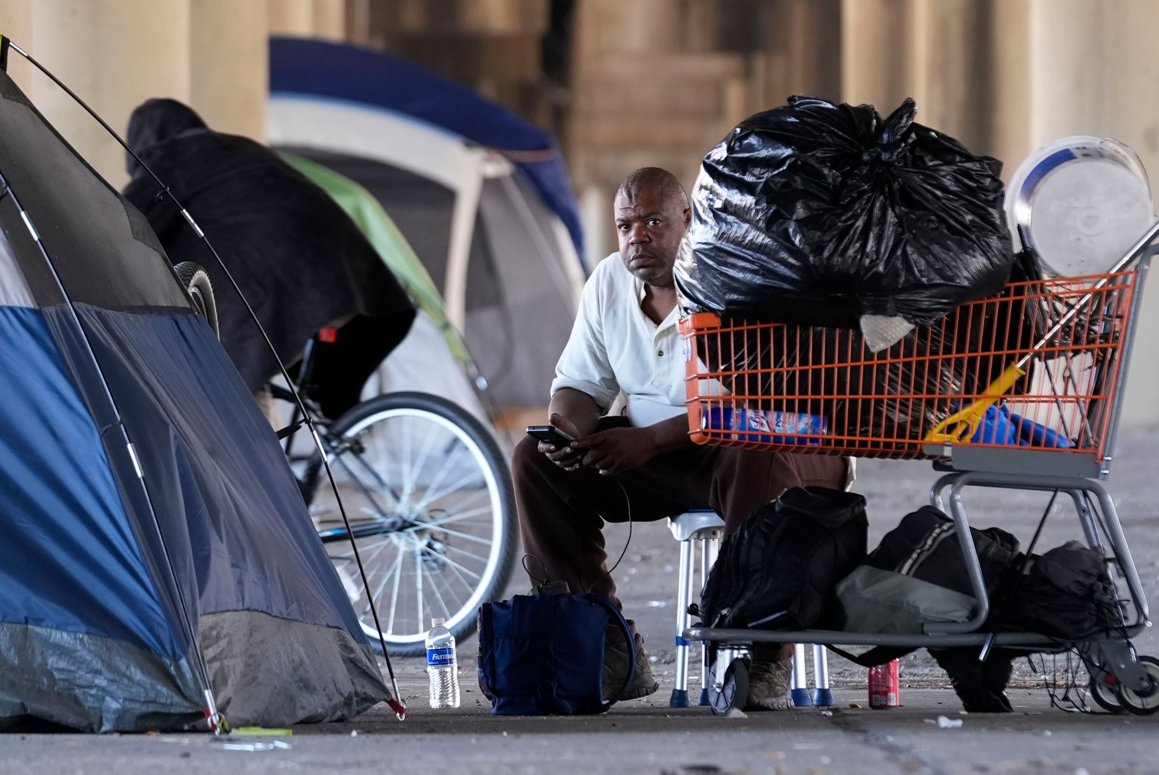 A man in a homeless encampment sits among possessions after Louisiana State police gave instructions for them to move to a different pre-designated location as they perform a sweep in advance of a Taylor Swift concert in New Orleans, Wednesday, Oct. 23, 2024. (AP Photo/Gerald Herbert)