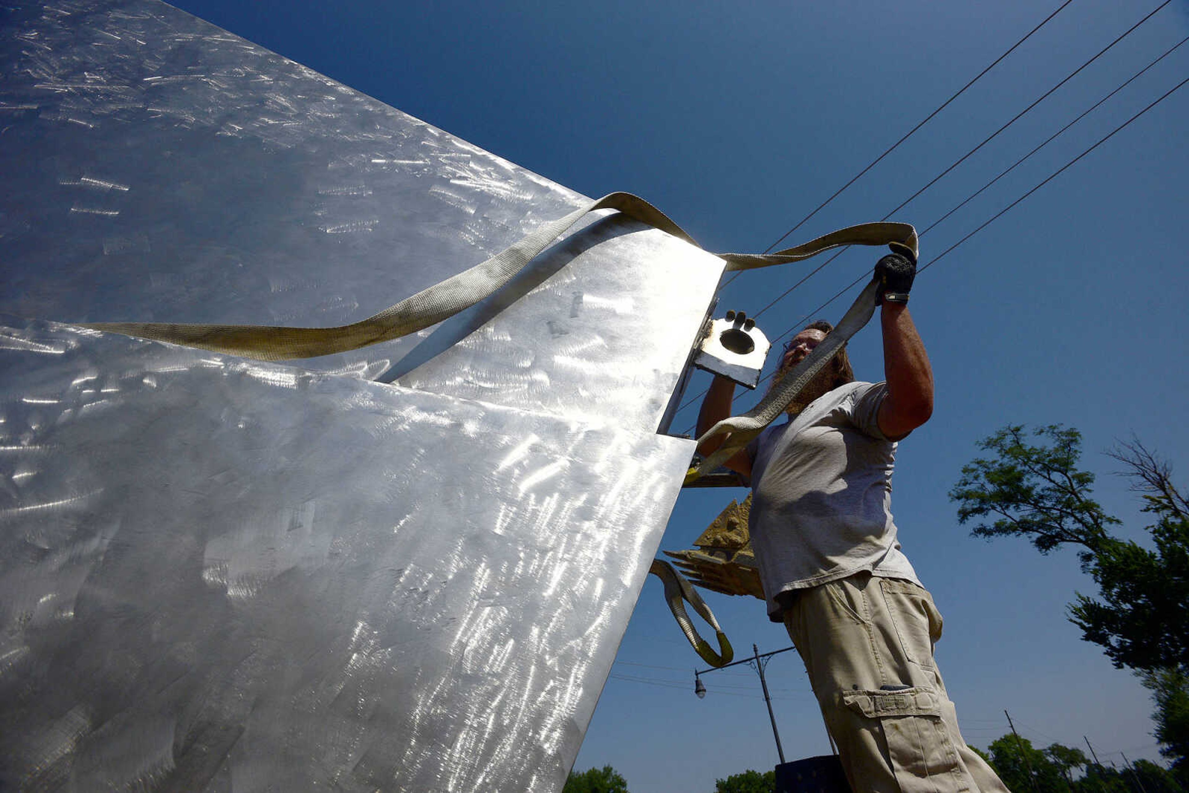 Joseph Ettling with the Cape Girardeau Parks and Recreation Department, removes a strap after the installation of the second piece of Chris Wubbena's 14-foot sculpture, "Commence", in the Fountain Street roundabout on Monday, July 24, 2017, near the River Campus in Cape Girardeau.