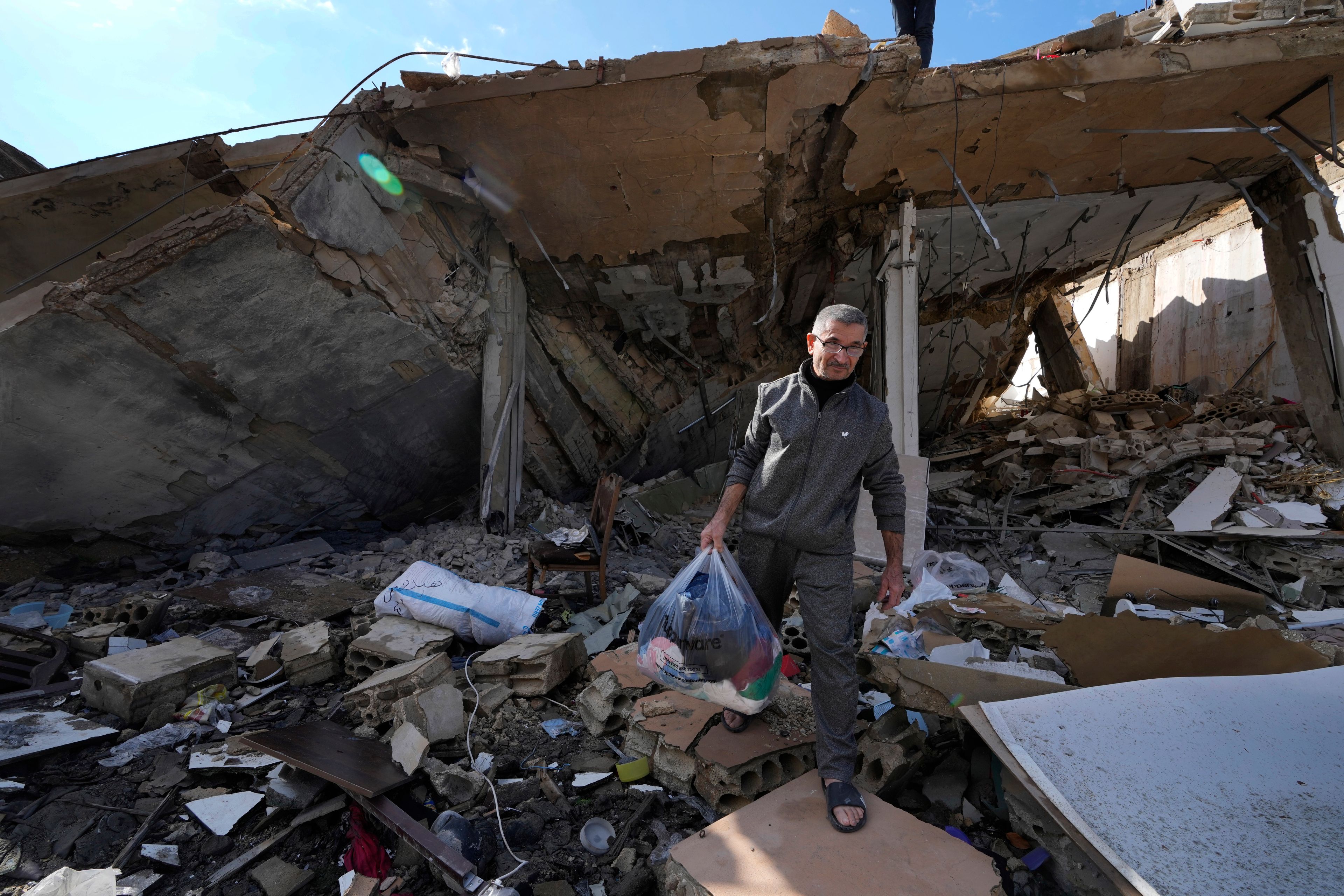 Ali Haidous carries a plastic bag with the remains of her family clothes, as he walks on the rubble of his destroyed house after he returned with his family to Hanouiyeh village, southern Lebanon, Thursday, Nov. 28, 2024 following a ceasefire between Israel and Hezbollah that went into effect on Wednesday.(AP Photo/Hussein Malla)