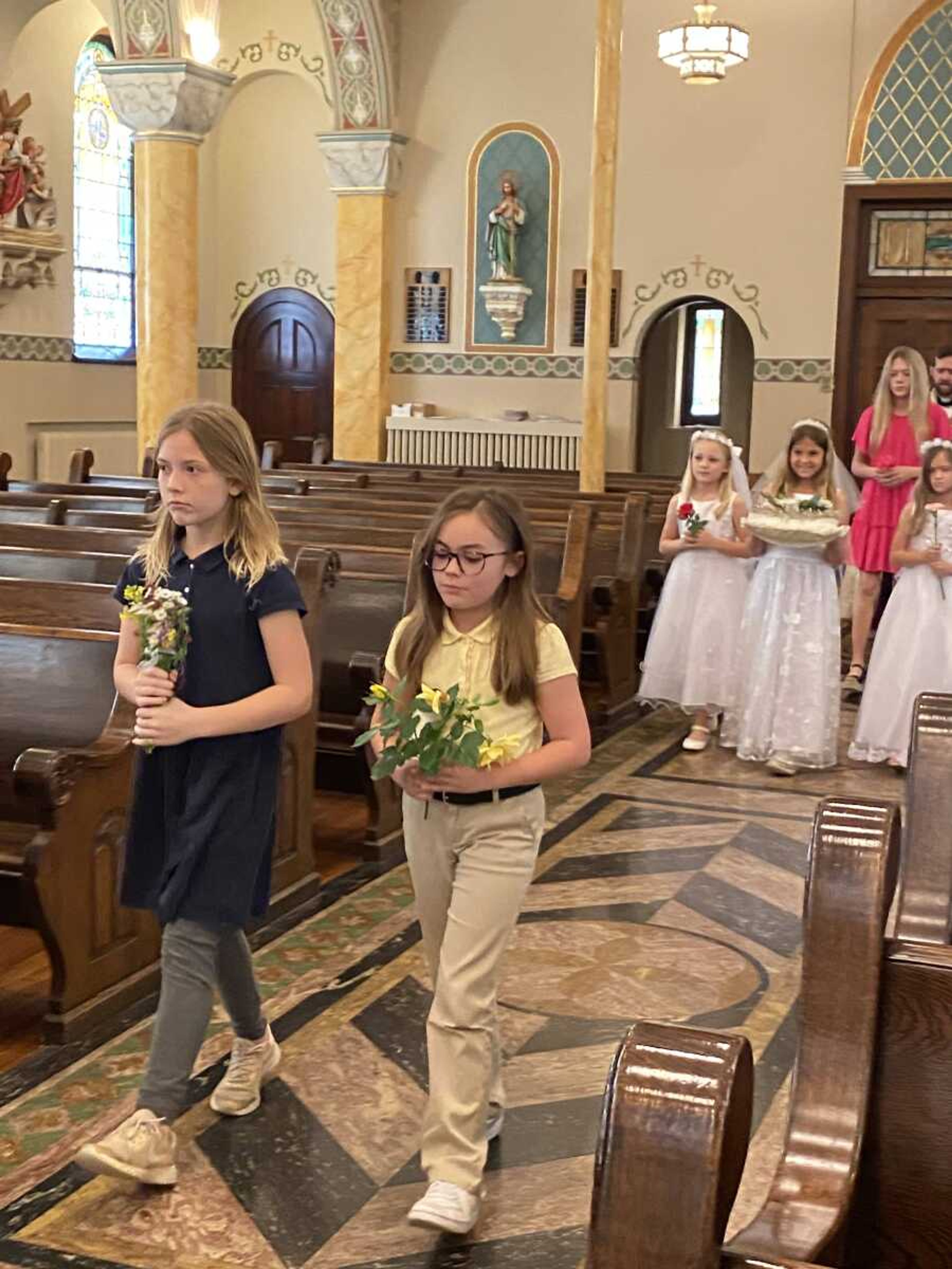 The 2nd grade girls, Ava Forehand, and Father Kelly process down the aisle, carrying their flowers and the crown of flowers that will be placed upon Mary's head.In front is Elizabeth David & Chloe Caudle.  The First Communicants are Andrea Pobst, Saydi Priggel, & Kambrie Seabaugh.