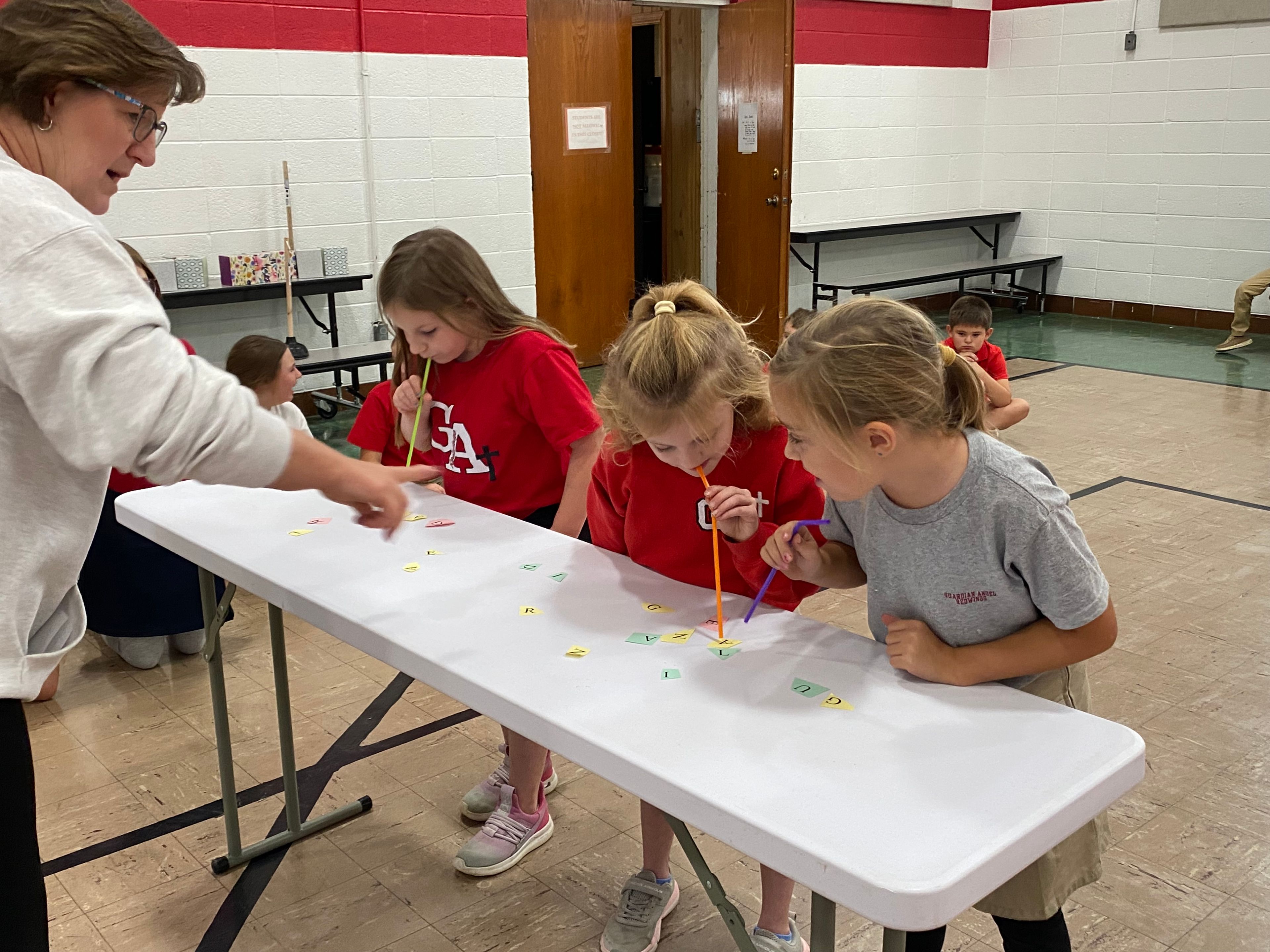 Clara Vetter, Teagan King, and Amelia Kyle of St. Gabriel's house use suction through a straw to pick up letters that will form the words "Guardian Angel" and “Gabriel".