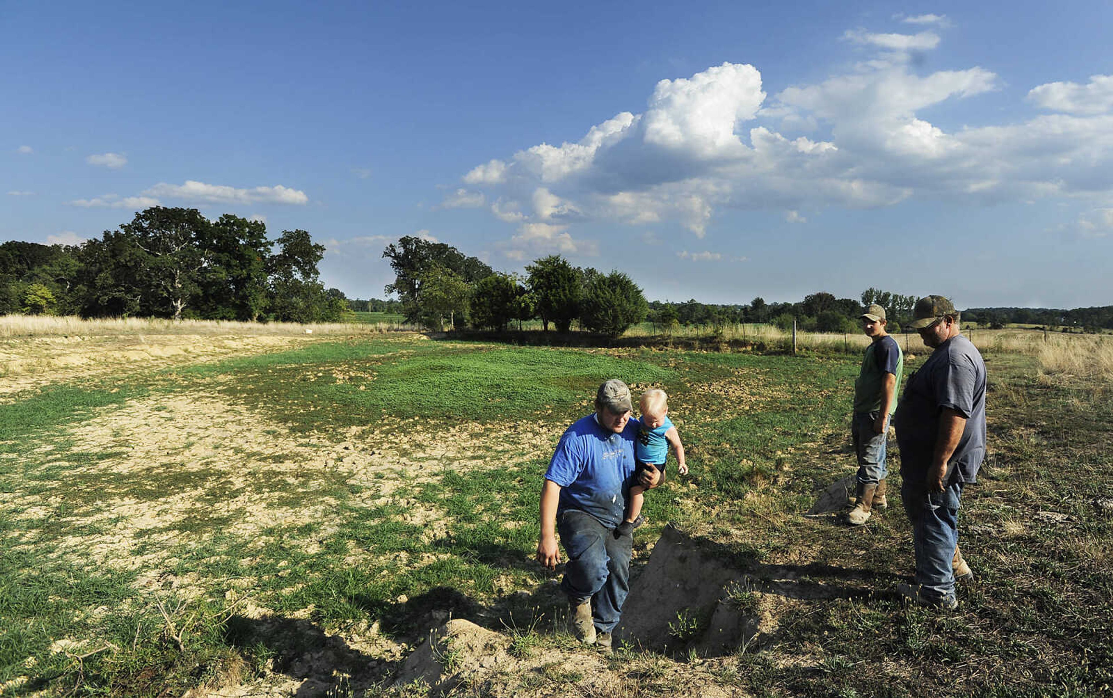 Chad and eighteen month-old Chase Kinder climb from the dry bed of a stock pond on his grandfather, right, Kirk Kinder's Daisy, Mo., farm while Chad's brother Cody, 15, watches Thursday, August 9. A work crew dug a new well on Kinder's farm with help from an emergency cost-share program through the State Soil and Water District Commission. Gov. Jay Nixon has directed $18.7 million in unallocated reserve funds to county soil and water districts to help livestock producers and farmers.