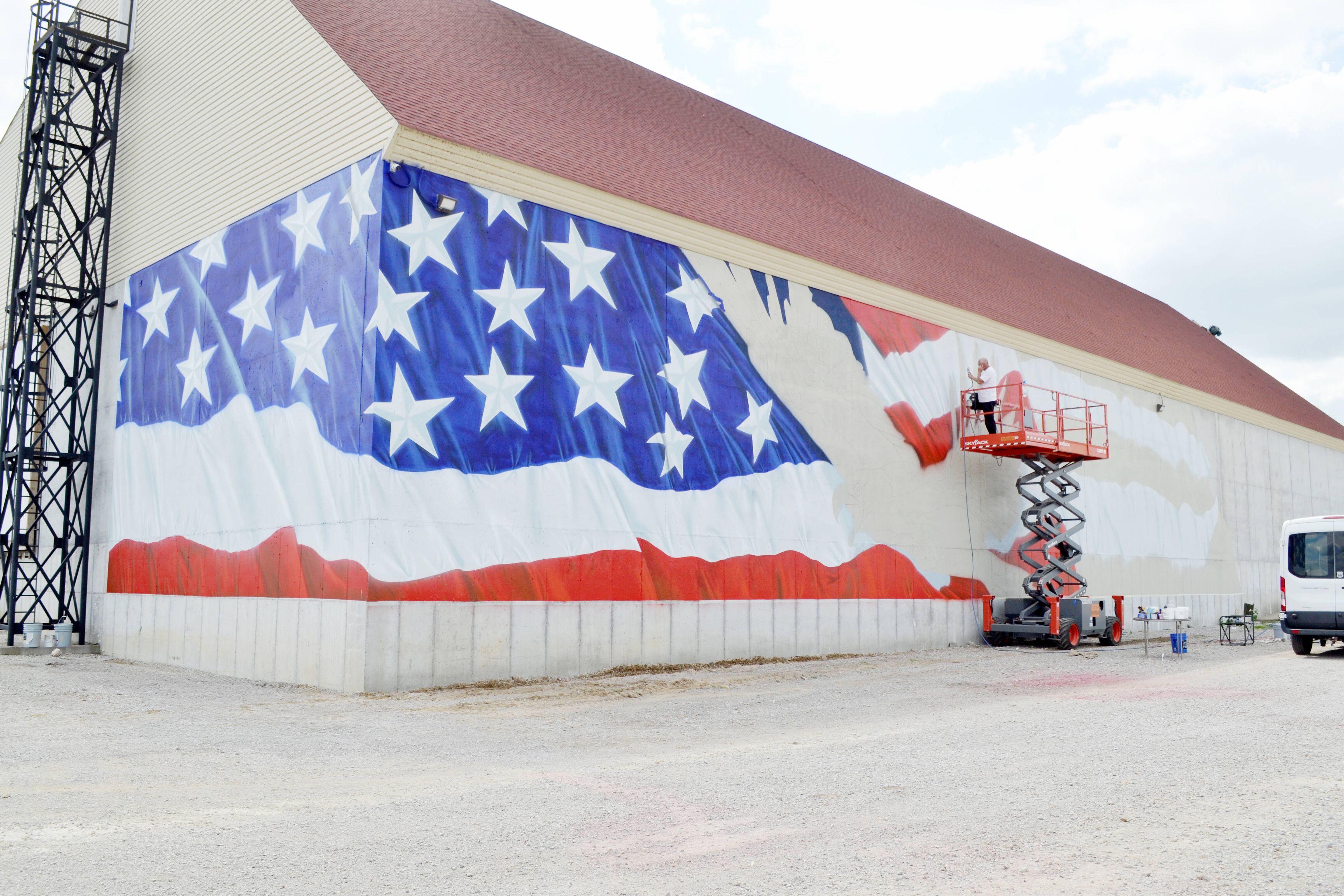 Artist Ray Harvey of New Haven paints the waving flag portion of the patriotic-themed mural on the north side of the Delta Growers Association building, located along Highway 105 in Charleston. The massive mural features a 139-foot waving flag and eagle and commemorates the 50th anniversary of the business.