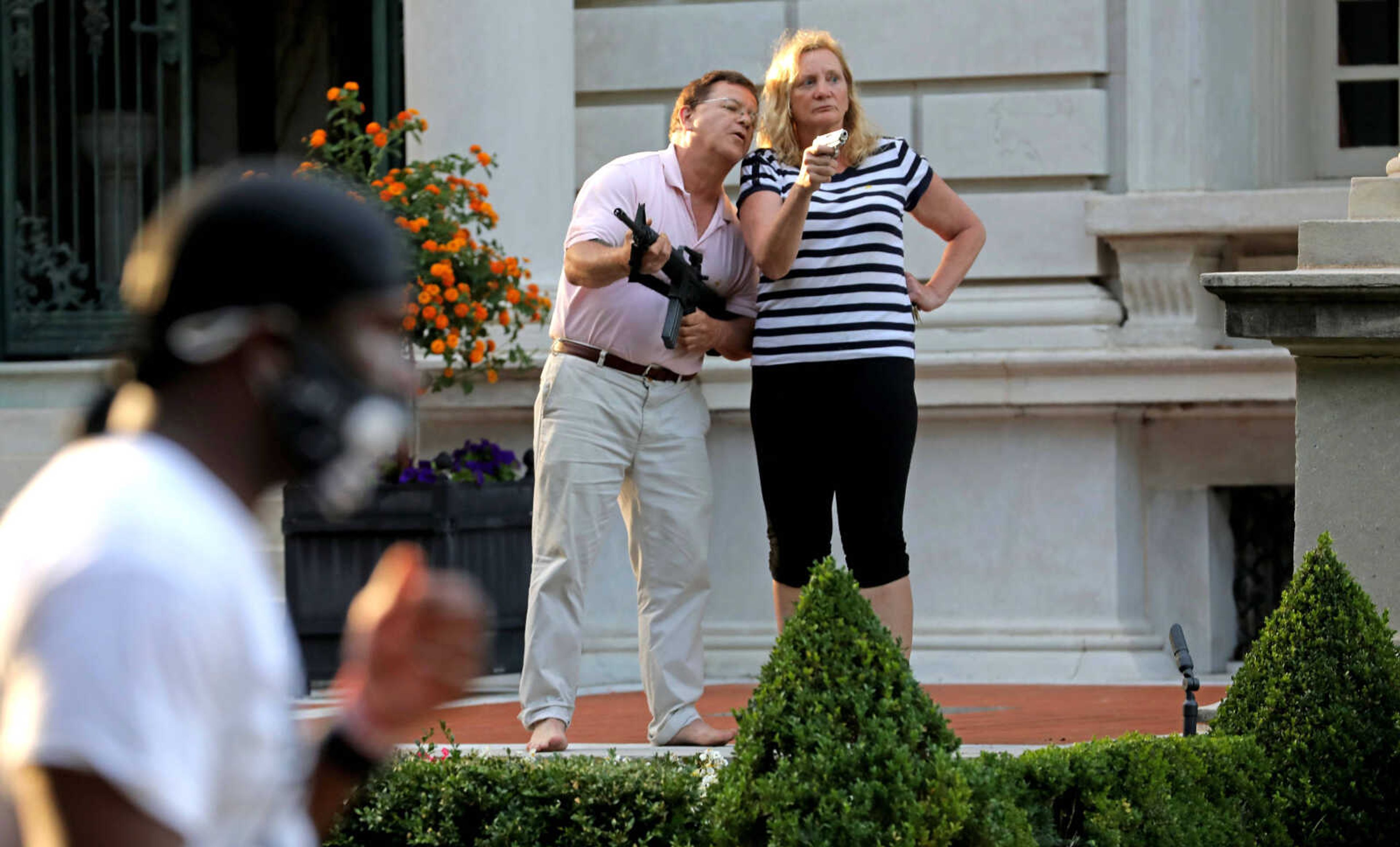 Armed homeowners Mark and Patricia McCloskey stand in front of their house, confronting protesters marching to St. Louis Mayor Lyda Krewson's house in the Central West End of St. Louis, June 28, 2020. A judge has expunged the misdemeanor convictions of the St. Louis couple who pointed guns at racial injustice protesters outside their mansion in 2020. Now, they say, they want their guns back. 