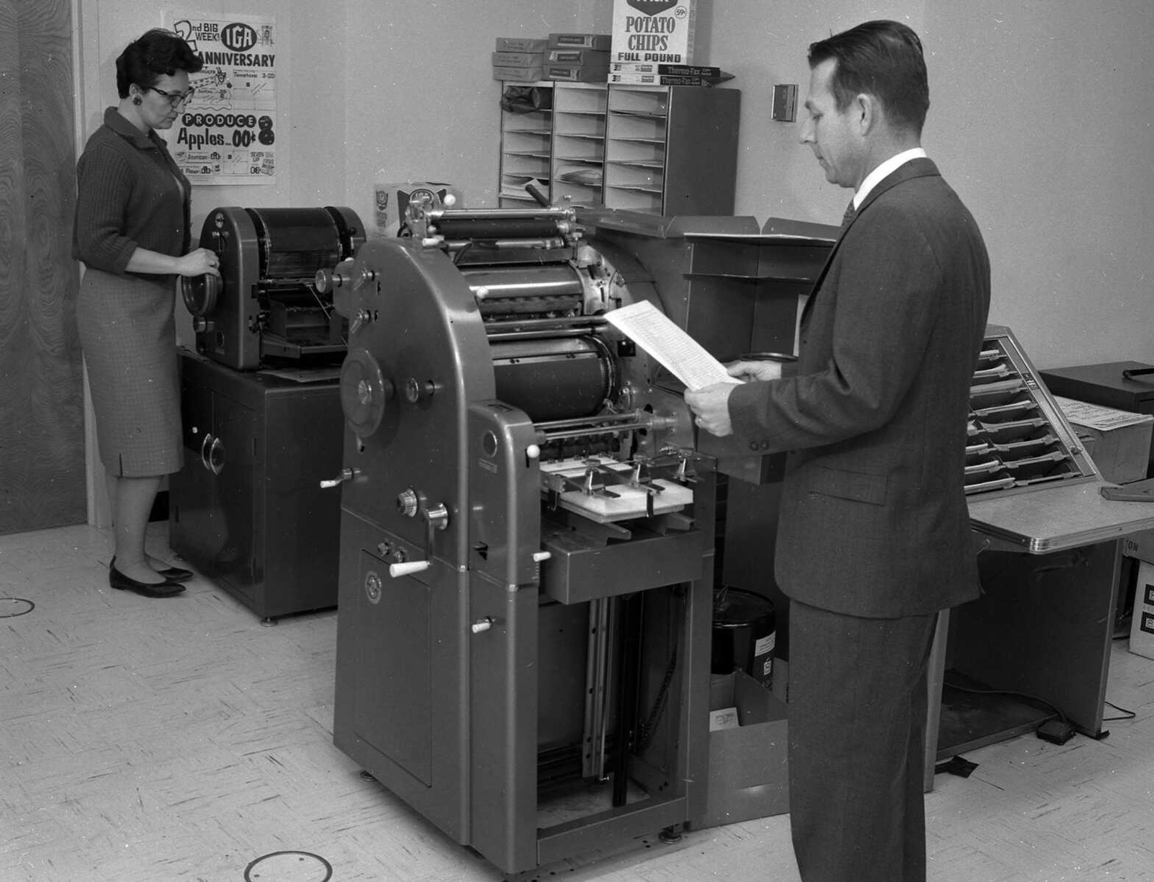 In this unidentified photo, a woman operates a mimeograph machine, while a man looks over what she has printed.