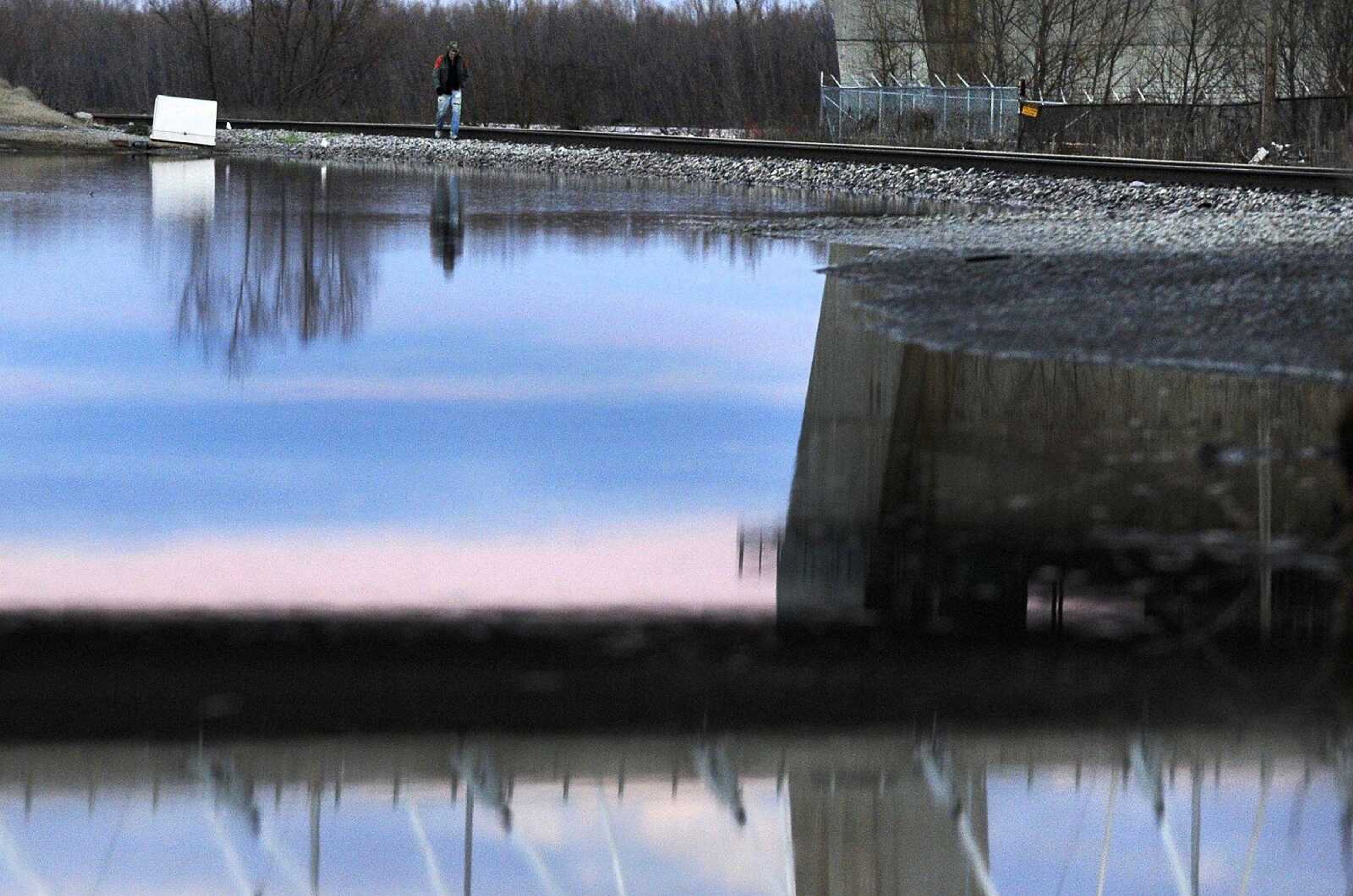 A man walking under the Bill Emerson Memorial Bridge is reflected Monday in receding floodwater along the train tracks near the Missouri Dry Dock in Cape Girardeau. (Laura Simon)