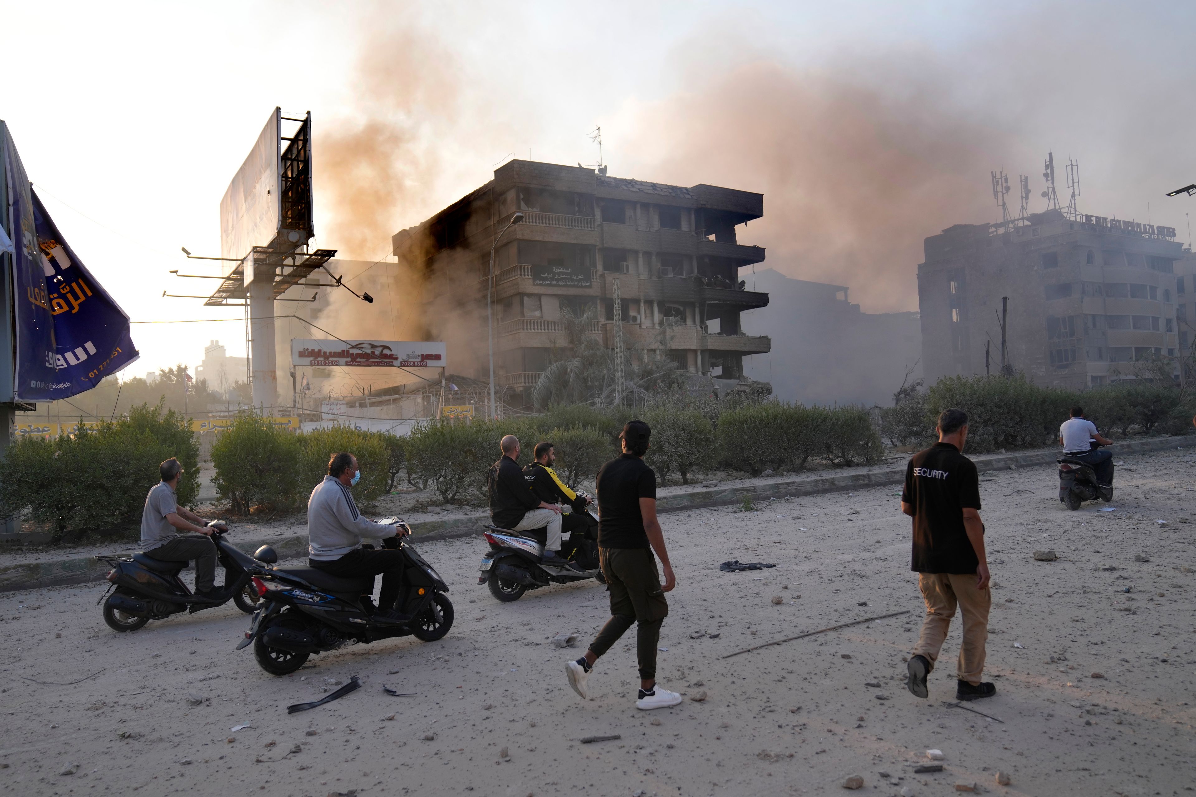 People pass in front of destroyed buildings that were hit by Israeli airstrikes in Dahiyeh, Beirut, Lebanon, Sunday, Oct. 6, 2024. (AP Photo/Hussein Malla)