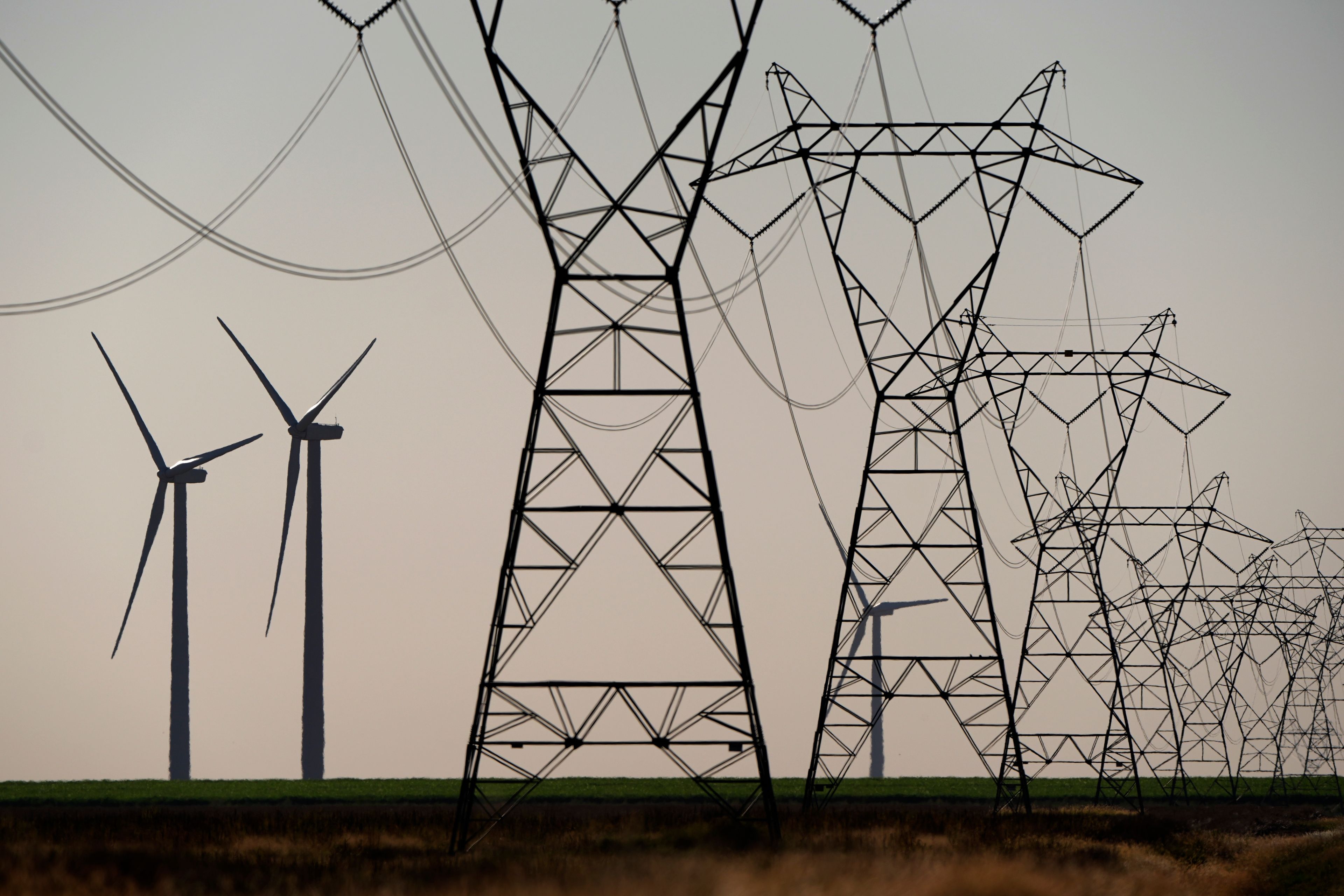 Wind turbines rise in the distance behind electric transmission lines at the Spearville Wind Farm, Sunday, Sept. 29, 2024, near Spearville, Kan. (AP Photo/Charlie Riedel)