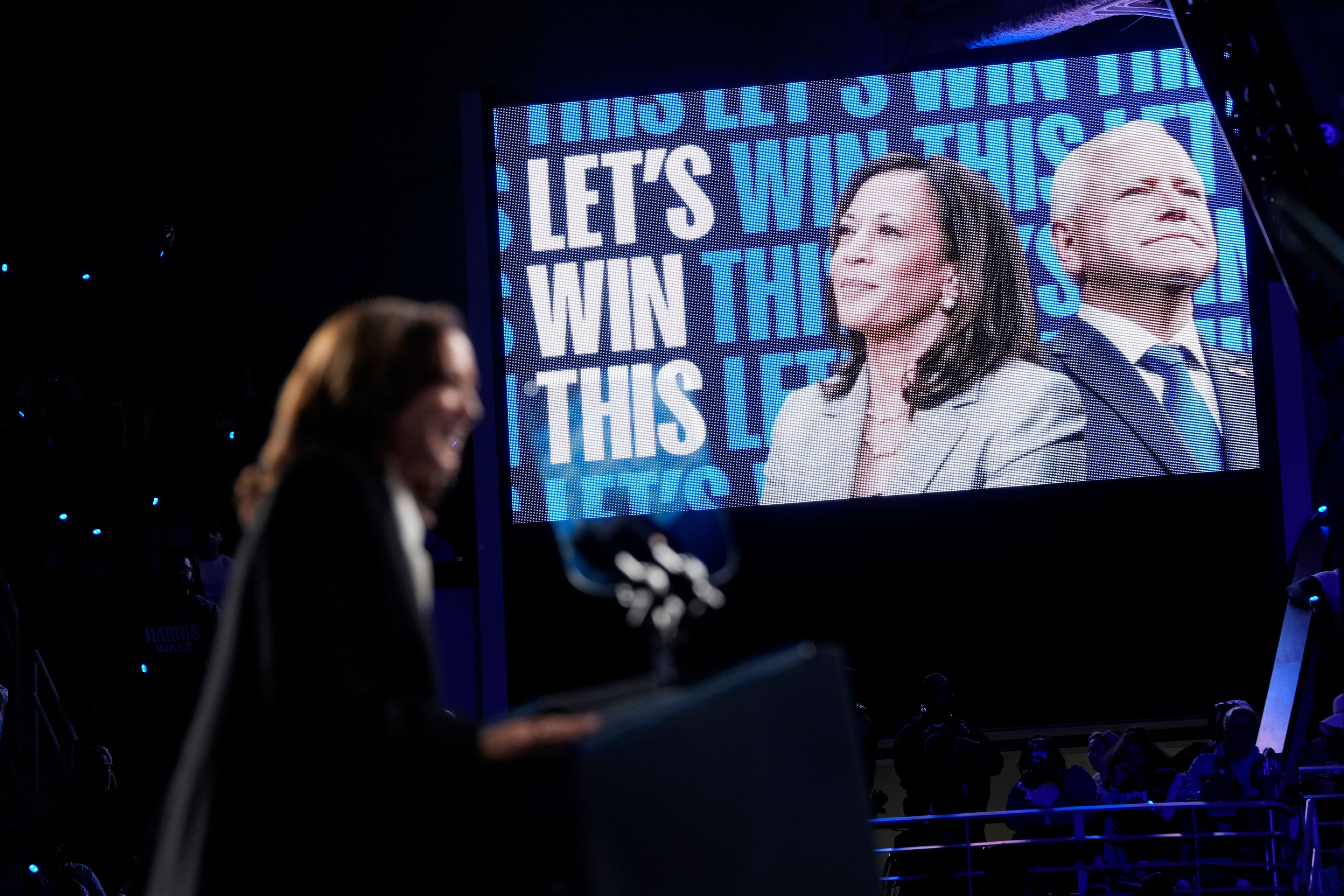 Democratic presidential nominee Vice President Kamala Harris, center, and her running mate Minnesota Gov. Tim Walz, right, appear on screen as Harris speaks at a campaign rally at East Carolina University in Greenville, N.C., Sunday, Oct. 13, 2024. (AP Photo/Susan Walsh)