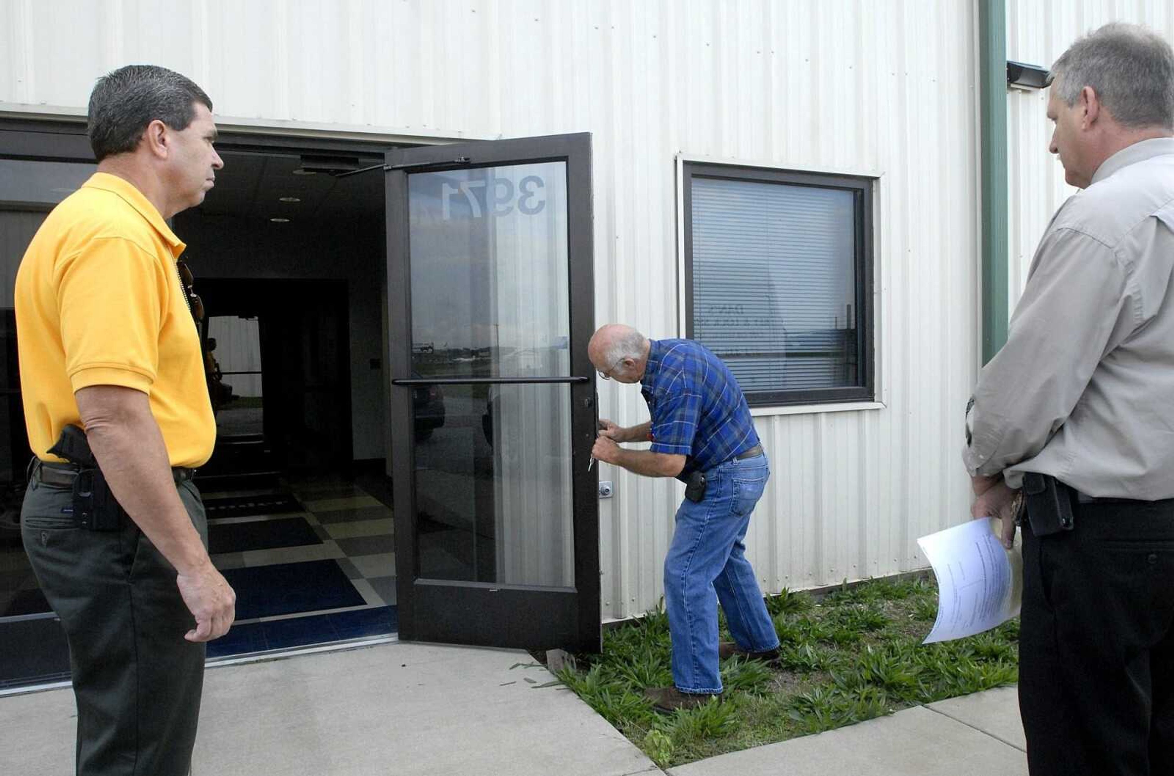 Lt. Jerry Bledsoe, left, and Capt. Gregg Ourth with the Scott County Sheriff's Department watch as Dan from Dan's Key and Lock Shop changes the locks on the main entrance of an airport hanger during the eviction of Commander Premier Wednesday morning, October 12, 2011 at the Cape Girardeau Regional Airport. (Laura Simon)