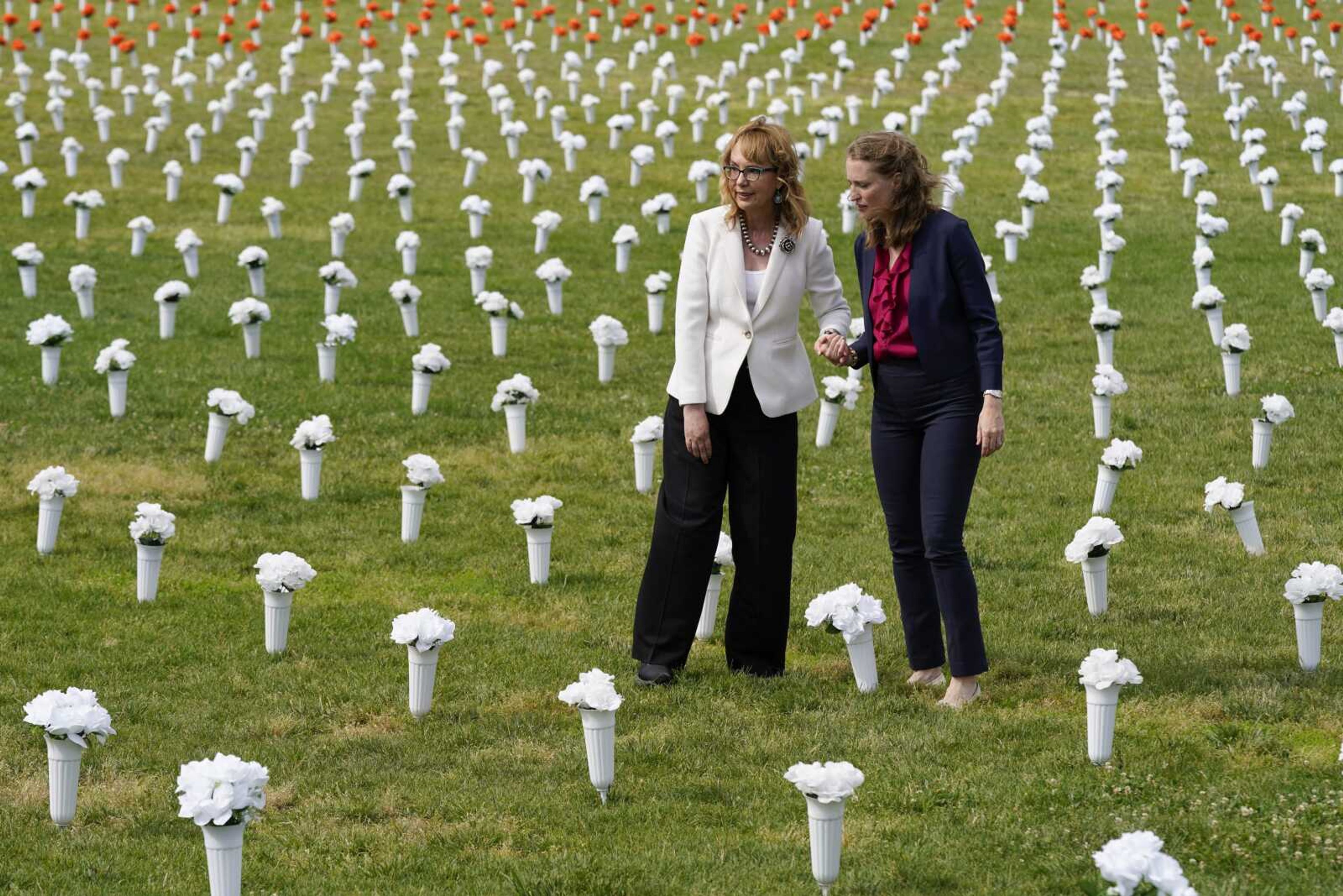 Former congresswoman and gun violence survivor Gabby Giffords, left, and Robin Lloyd, managing director of Giffords, walk Tuesday among vases of flowers of the Gun Violence Memorial installation on the National Mall in Washington. The flowers are meant to represent the number of Americans who die from gun violence each year.