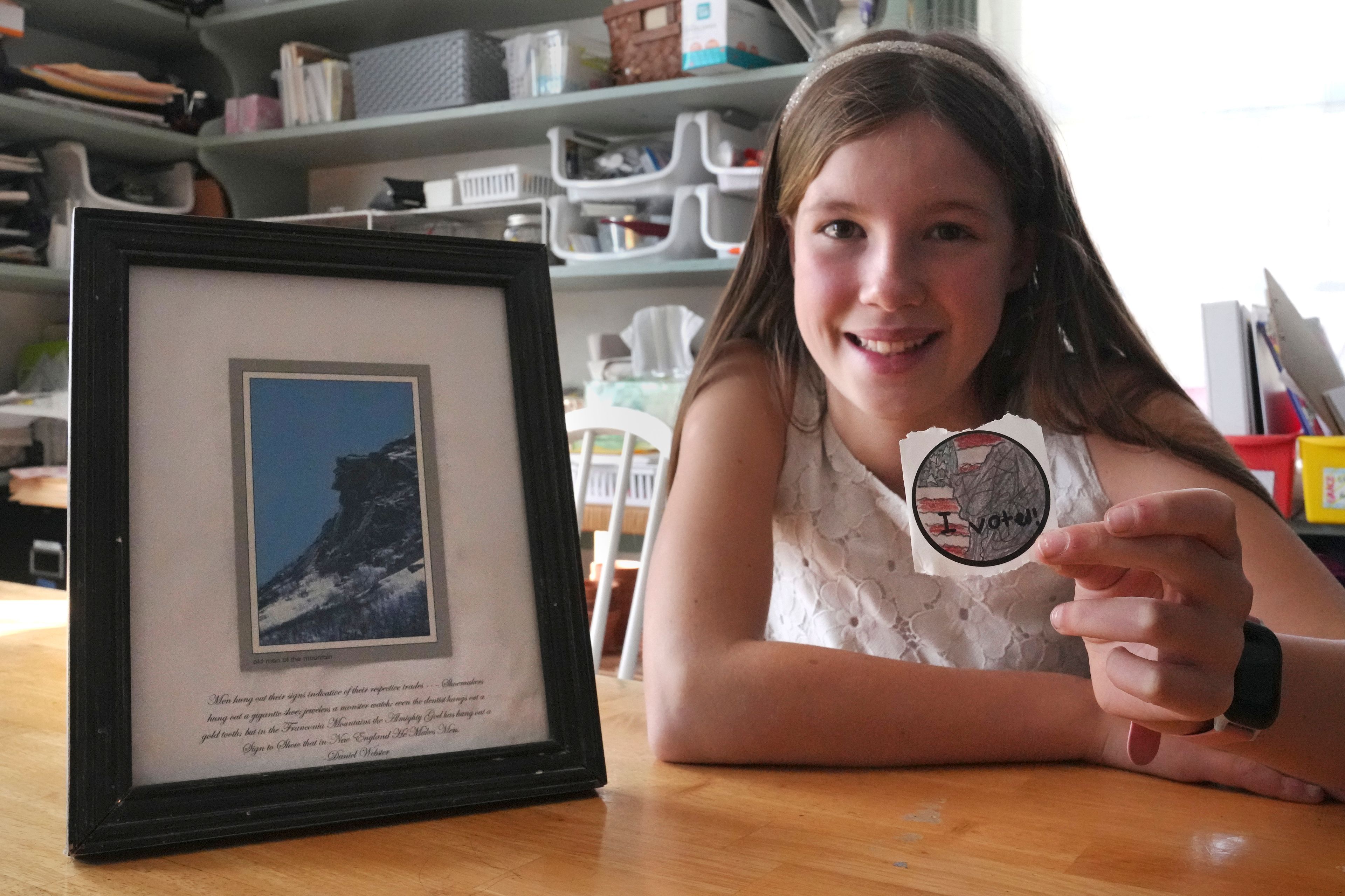 Ten-year-old Grace, of Milton, N.H. shows her contest winning "I Voted" sticker in her homeschool classroom, Thursday, Oct. 31, 2024, in Milton. Grace's design, inspired by the framed image of New Hampshire's famed Old Man of the Mountain at her home, features the landmark with an American flag in the background. (AP Photo/Charles Krupa)