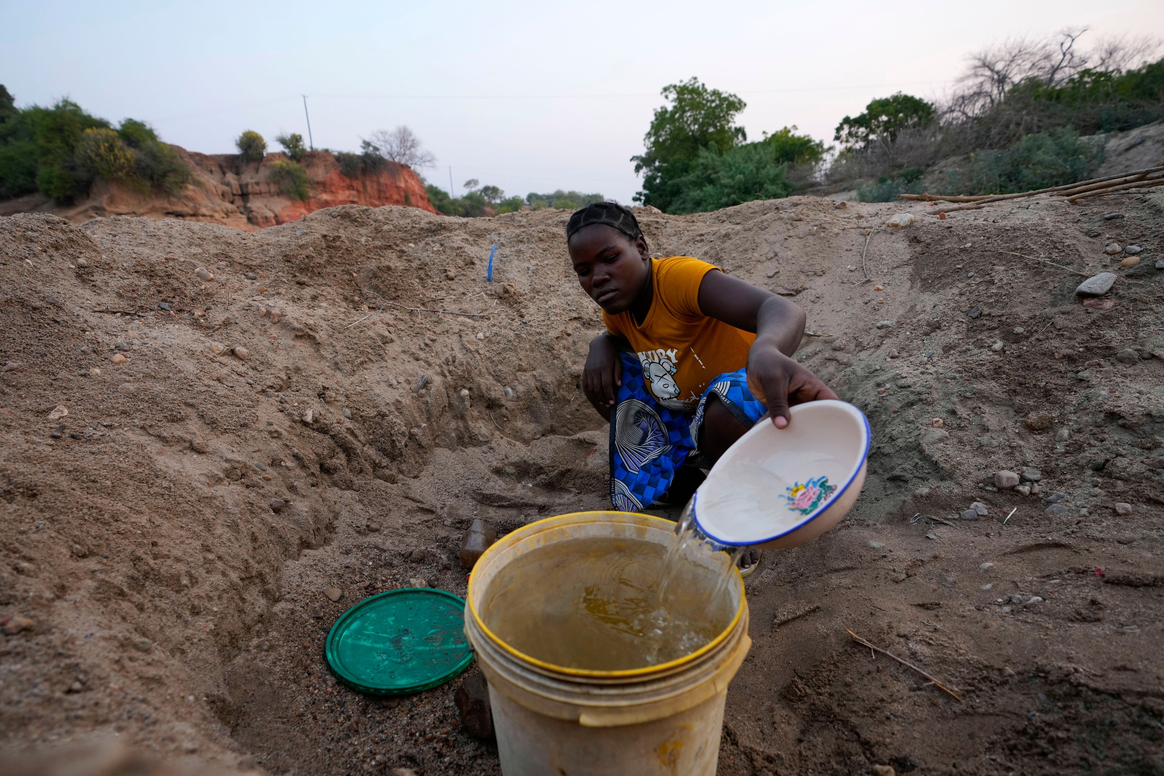 A woman scoops water from a hole she has dug in a dried up riverbed in Lusitu, Zambia, Wednesday, Sept. 18, 2024. (AP Photo/Themba Hadebe)