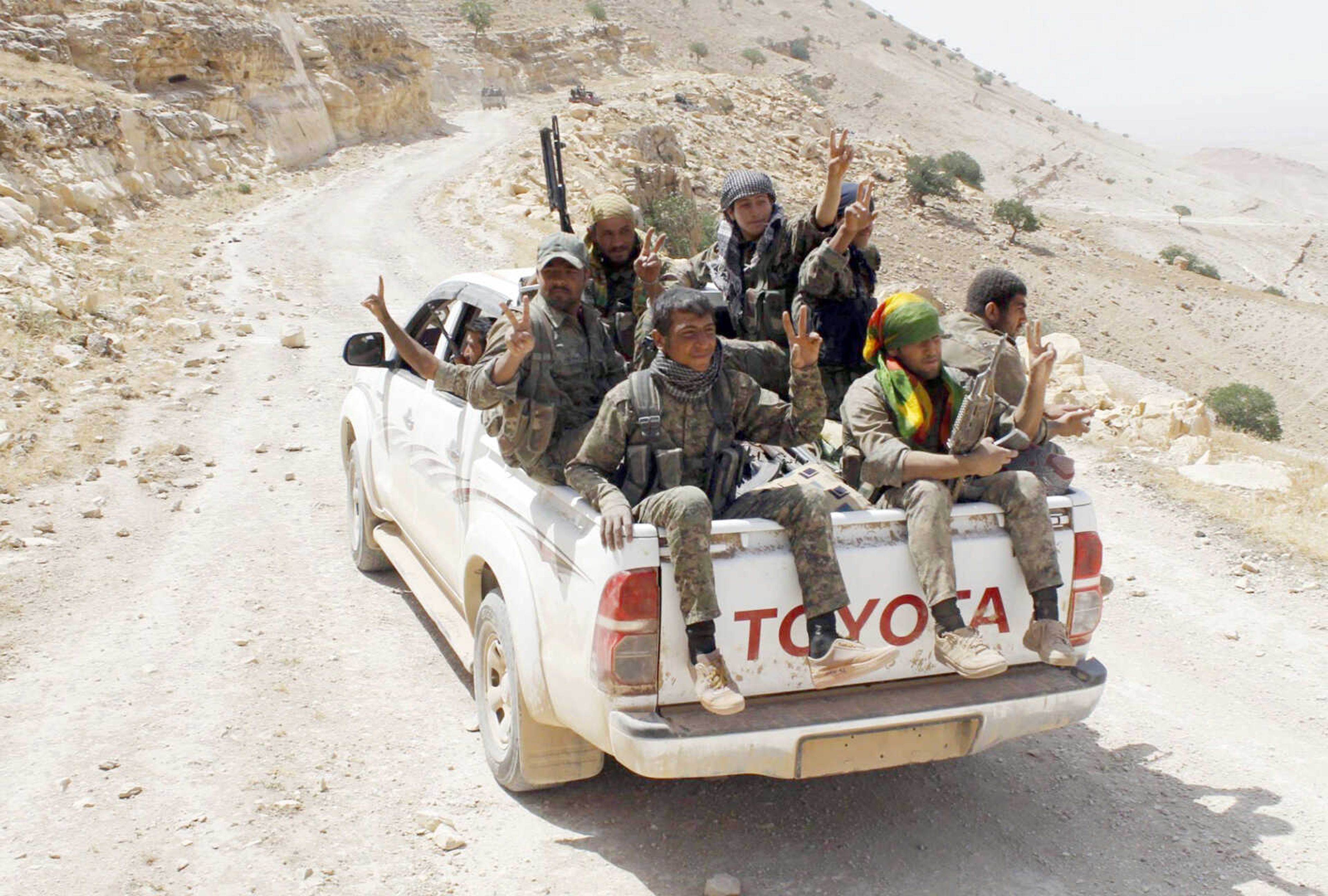 Kurdish fighters of the People's Protection Units, or YPG, flash victory signs as they sit on their pickup on their way to battle against the Islamic State on May 20 near Kezwan mountain in northeast Syria. (The Kurdish fighters of the People's Protection Units via AP, file)